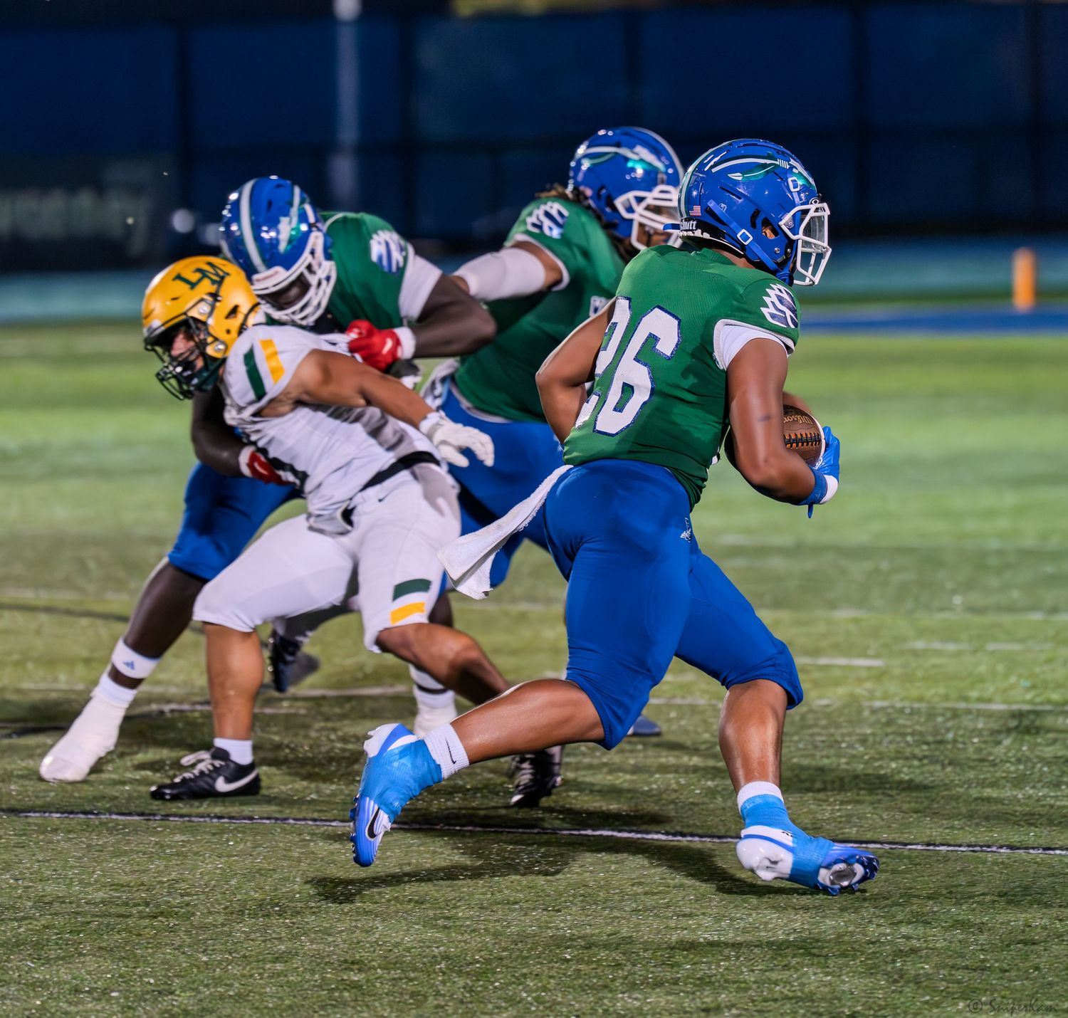 A blue and green uniformed player number 26 runs with the ball during a night game.