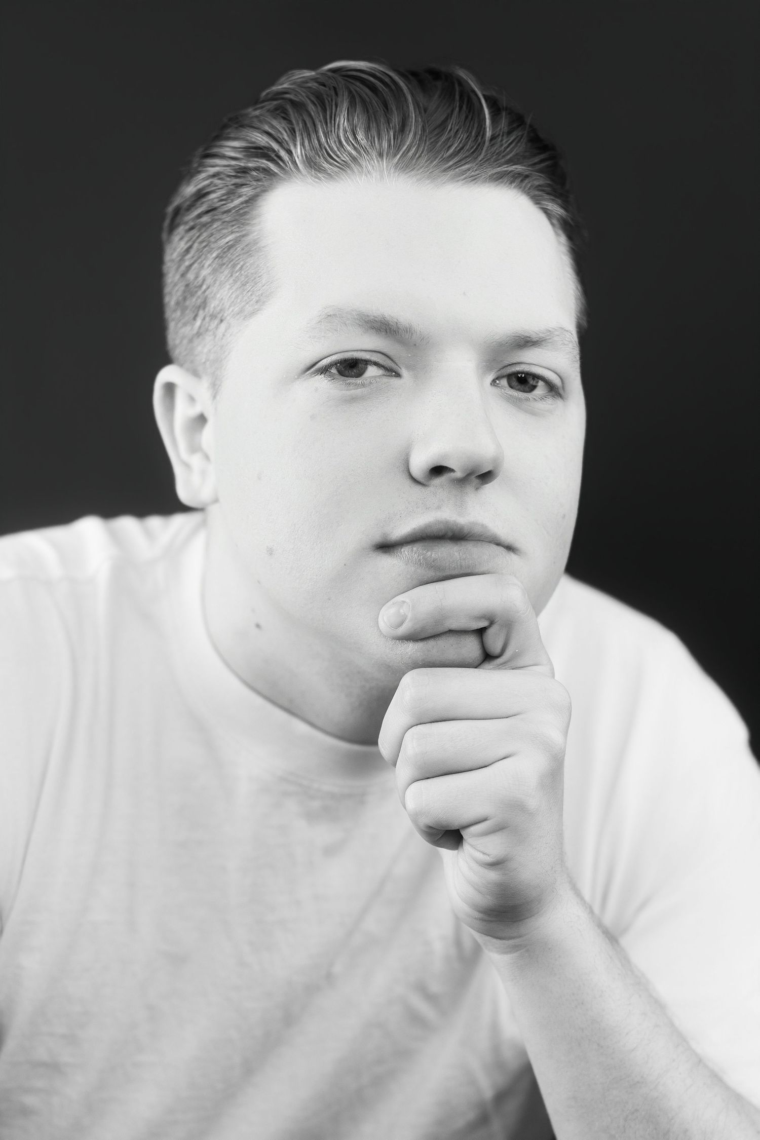 Black and white portrait of young man in white t-shirt with chin resting on fist.