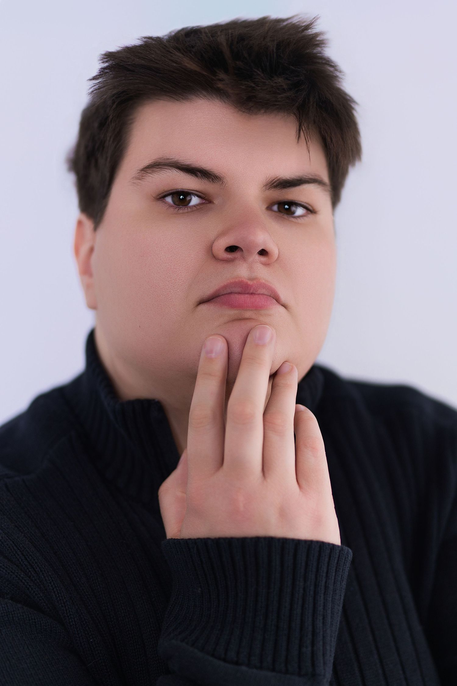 Thoughtful young person in black sweater resting hand on chin in a contemplative pose.
