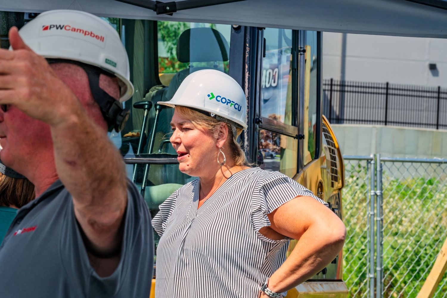 Woman in COPFCU hard hat observing construction site activities near heavy equipment.
