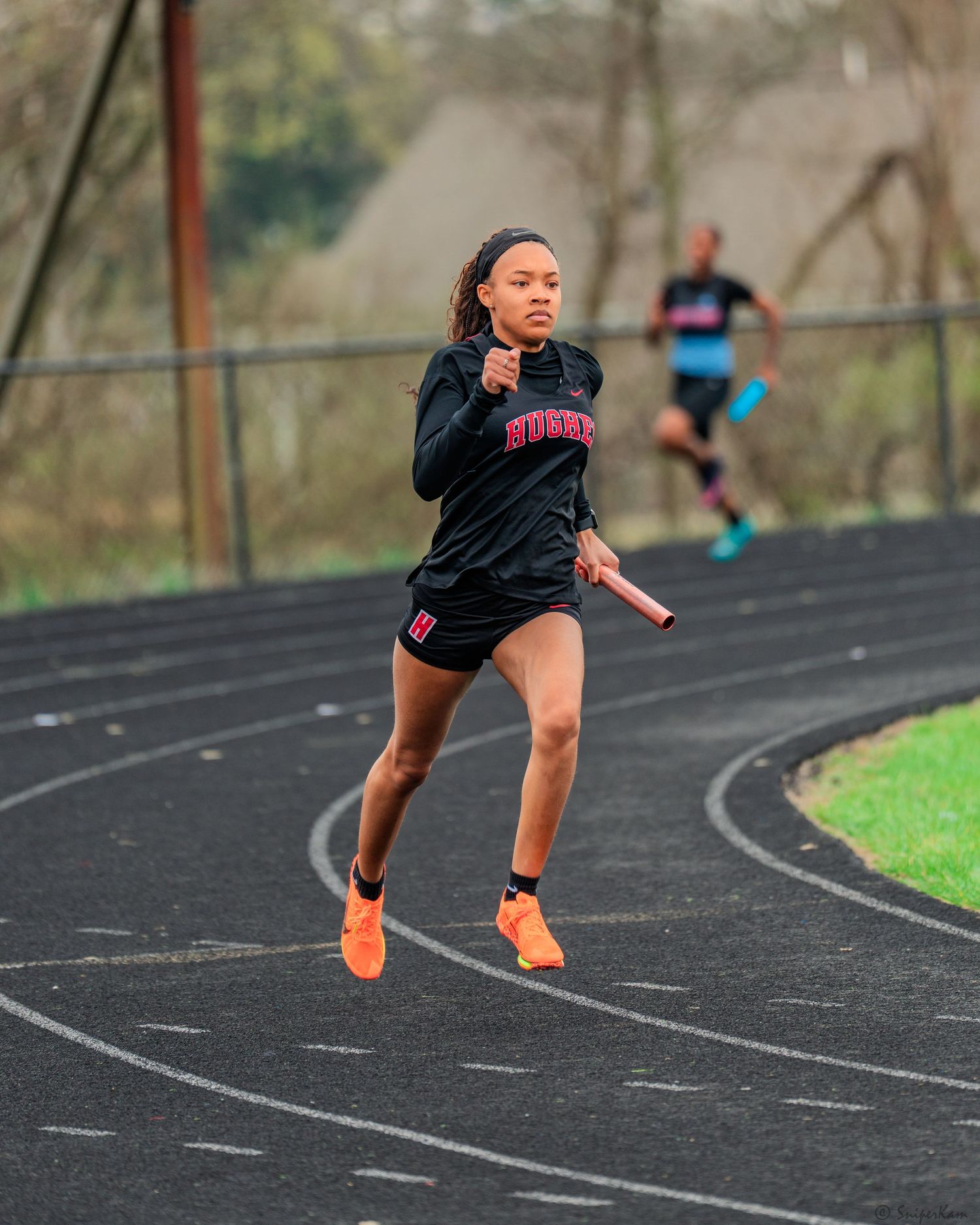 Female runner in black Hurley uniform sprinting on a track during a relay race.