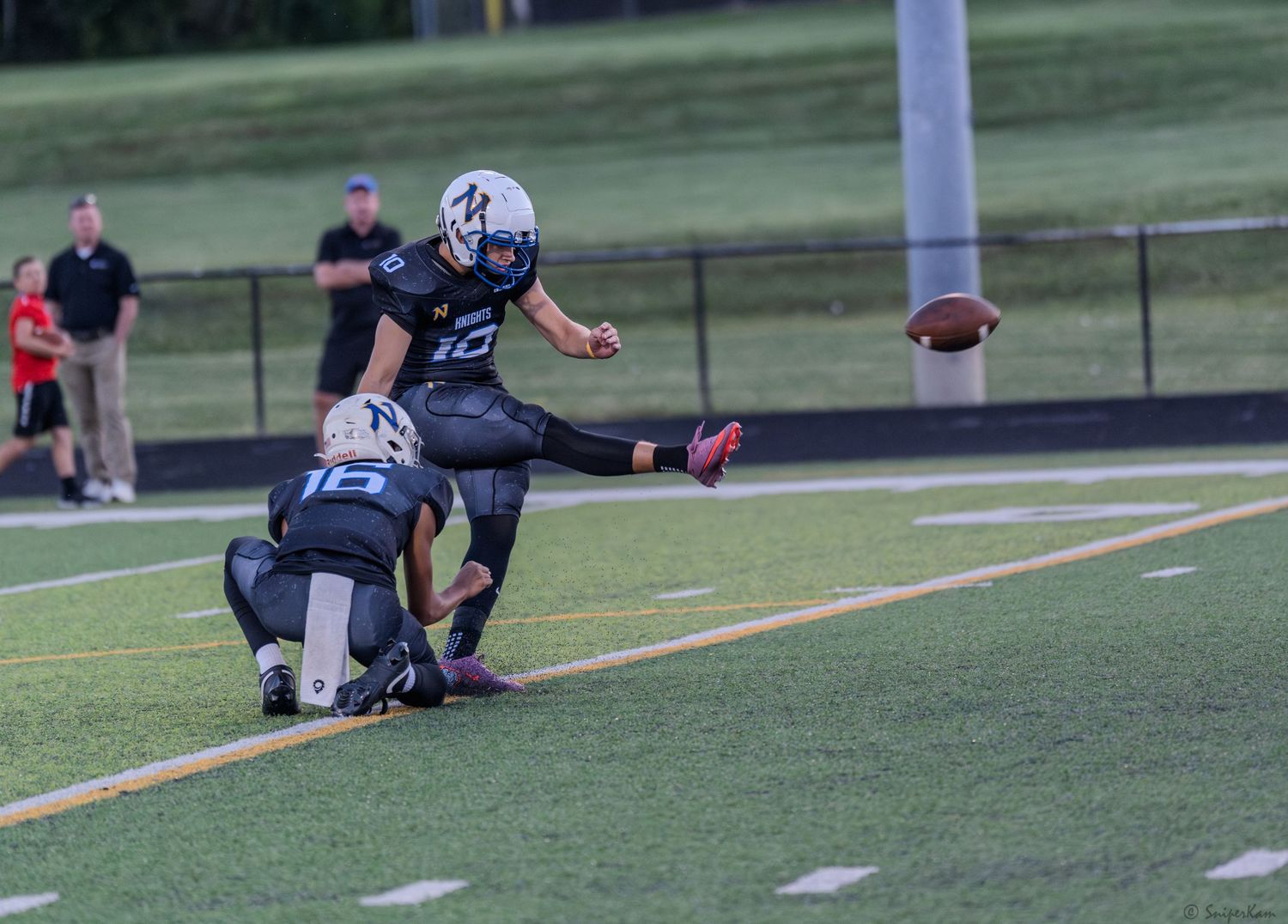 Football player wearing number 12 executes a kick during a game on a turf field.