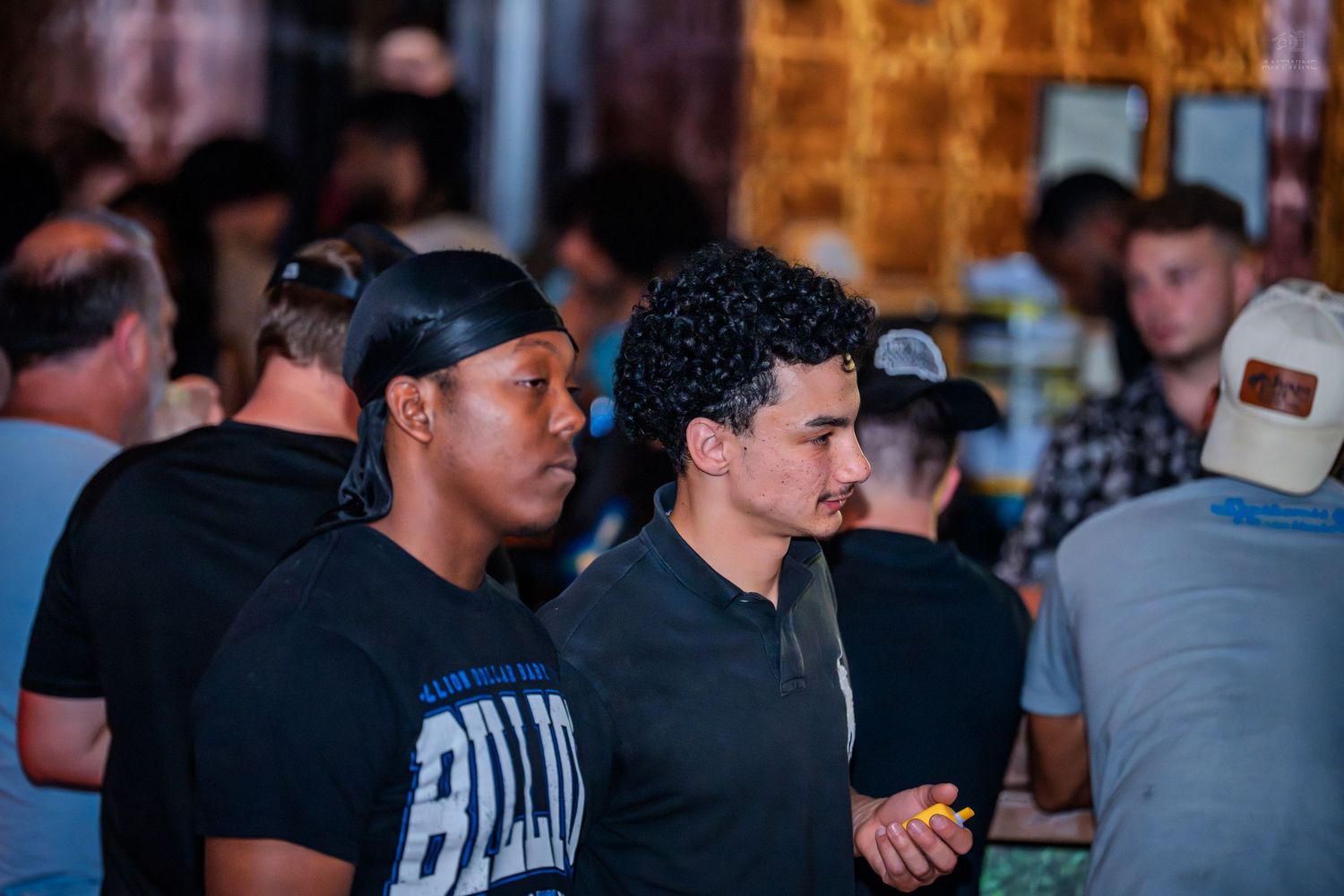 Two men standing together in a crowded nightclub venue, one wearing a blue shirt.