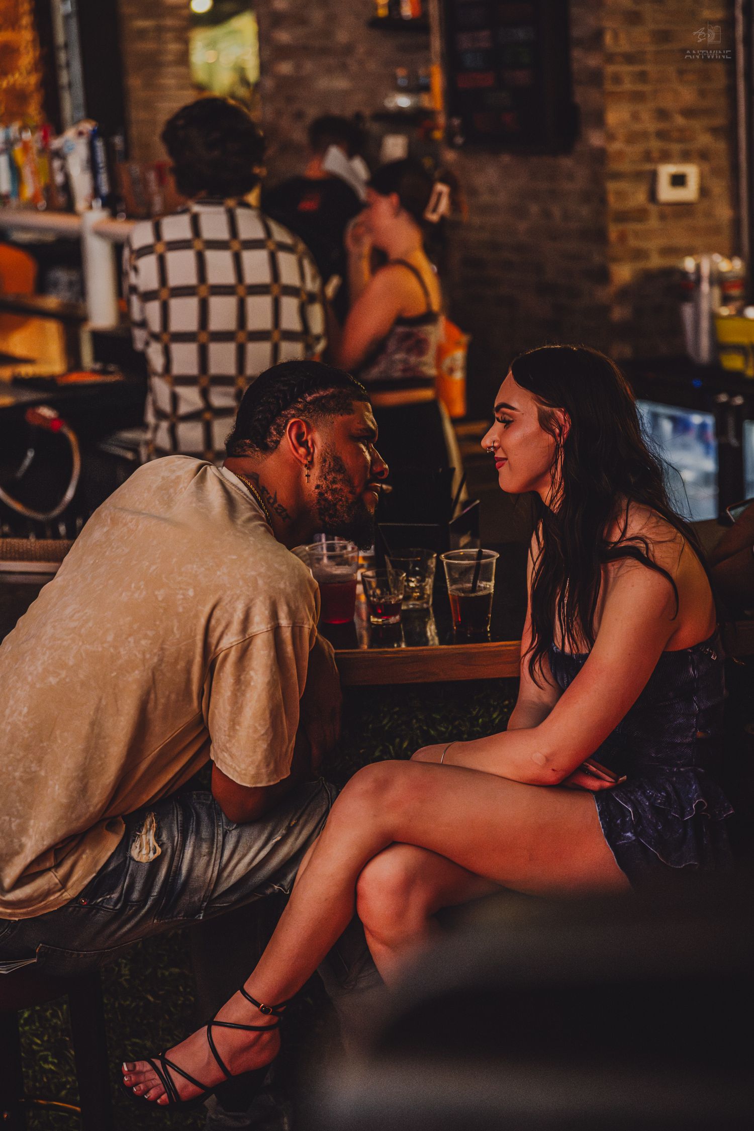 Couple gazes at each other intimately while seated at a cozy bar.