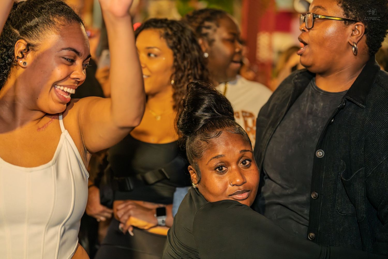 Group of women laughing and embracing while enjoying an outdoor nighttime social gathering.