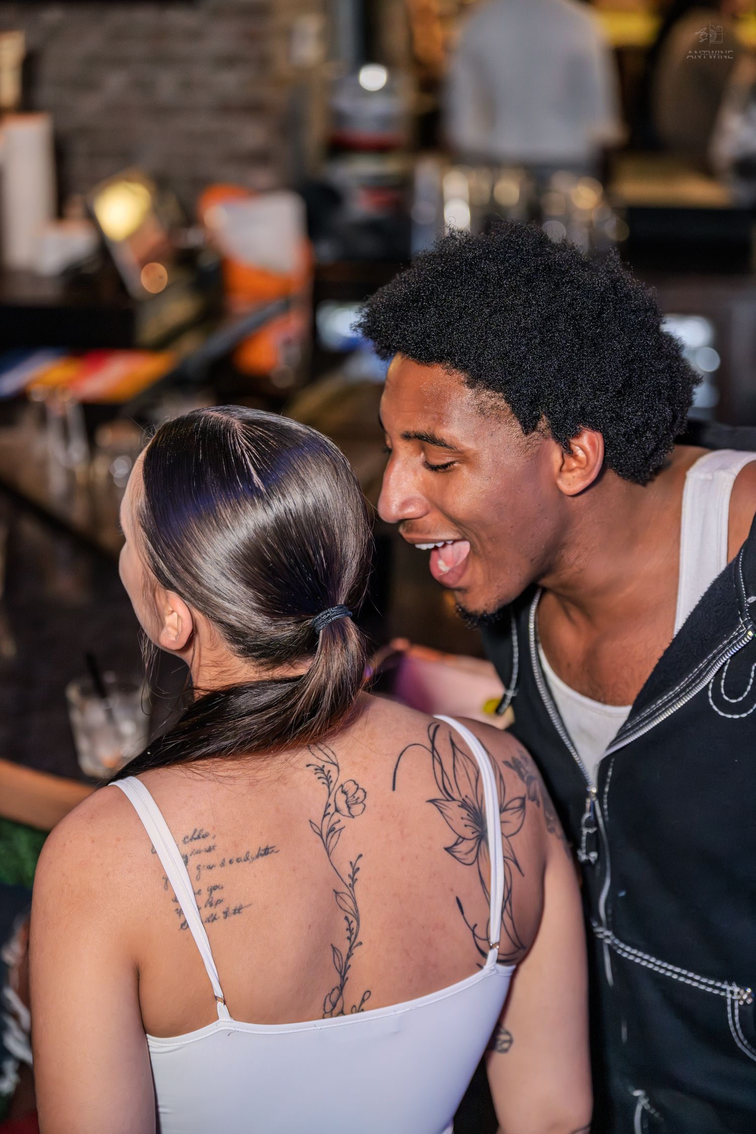 Young couple smiling together at a bar, woman showing back tattoos.
