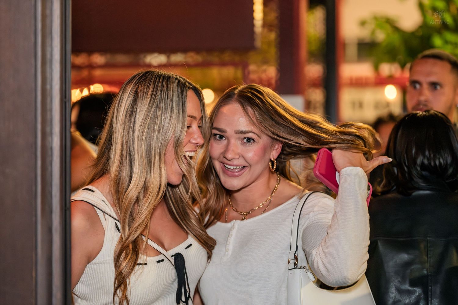 Two smiling women in white outfits pose together at a nighttime outdoor social event.