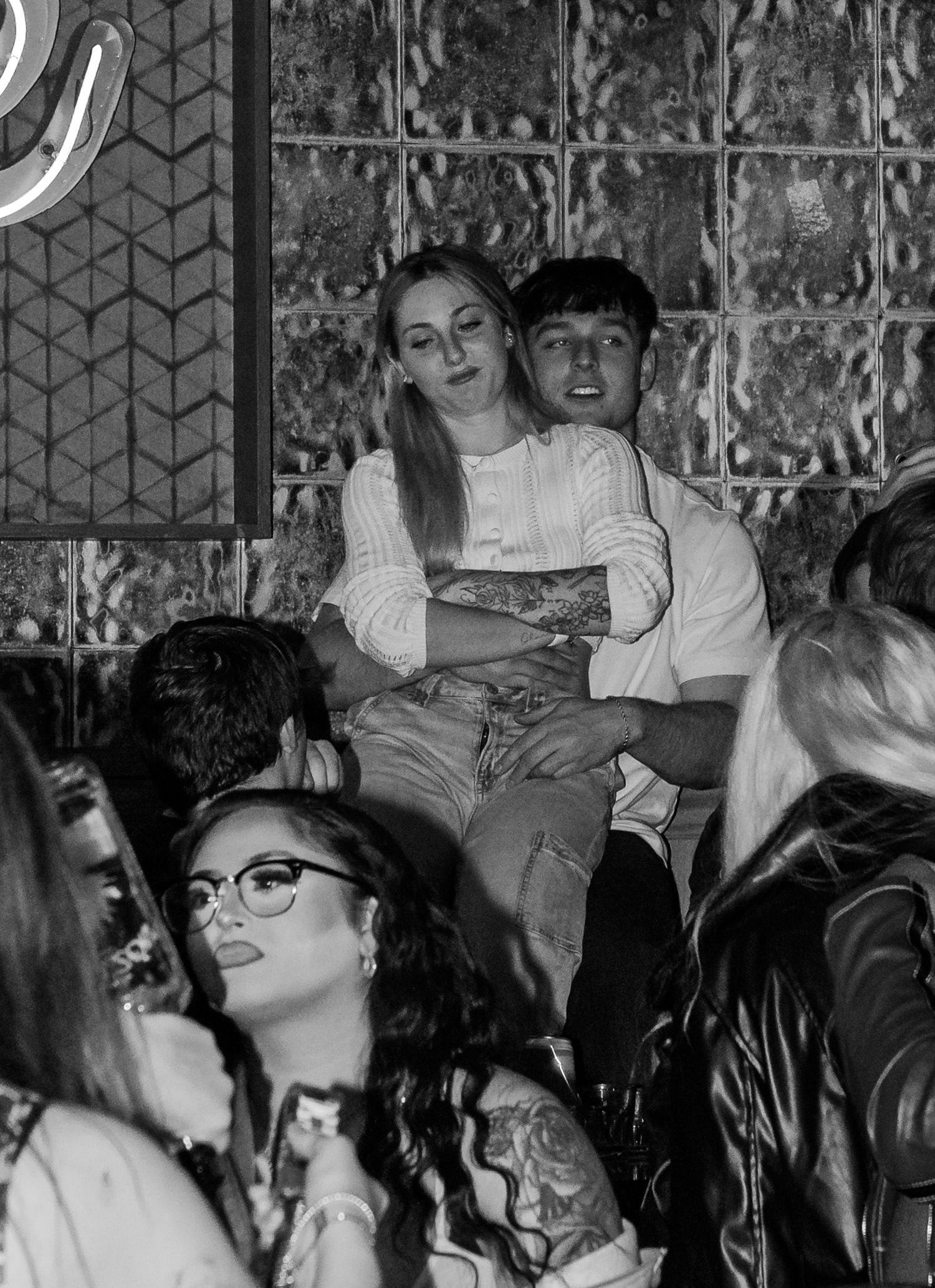 Black and white photo of a couple sitting together elevated above a nightclub crowd.