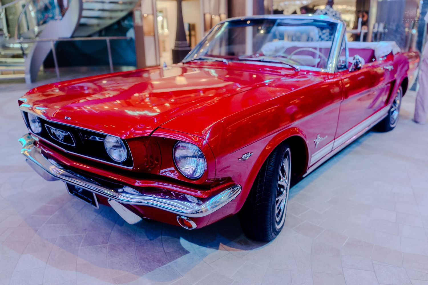 A classic red Ford Mustang convertible on display inside a luxury cruise ship atrium.