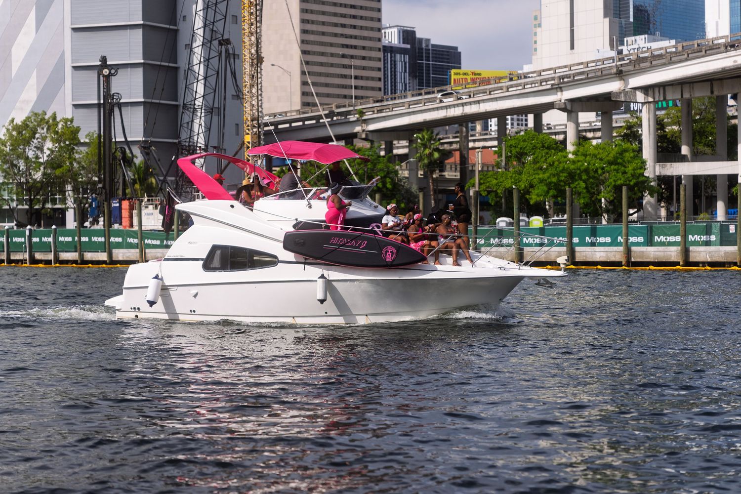 A white motor yacht with a pink party boat on its deck cruising through an urban waterway.