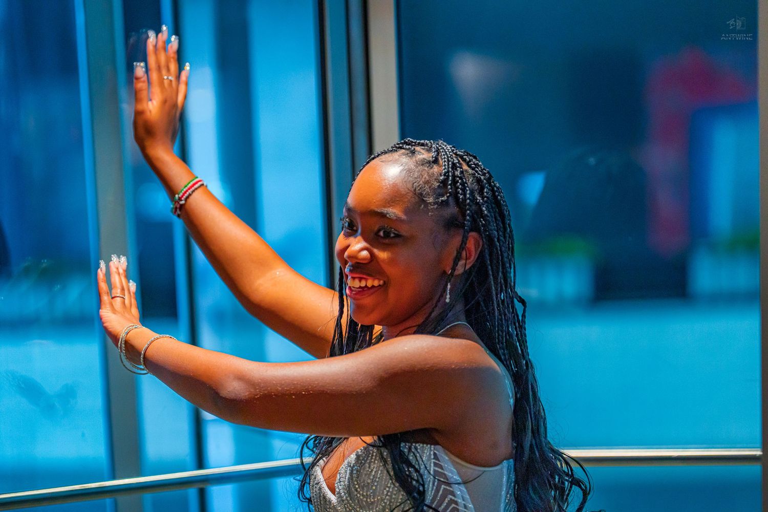 Young woman with braided hair smiling and posing against a blue-lit glass wall outdoors.