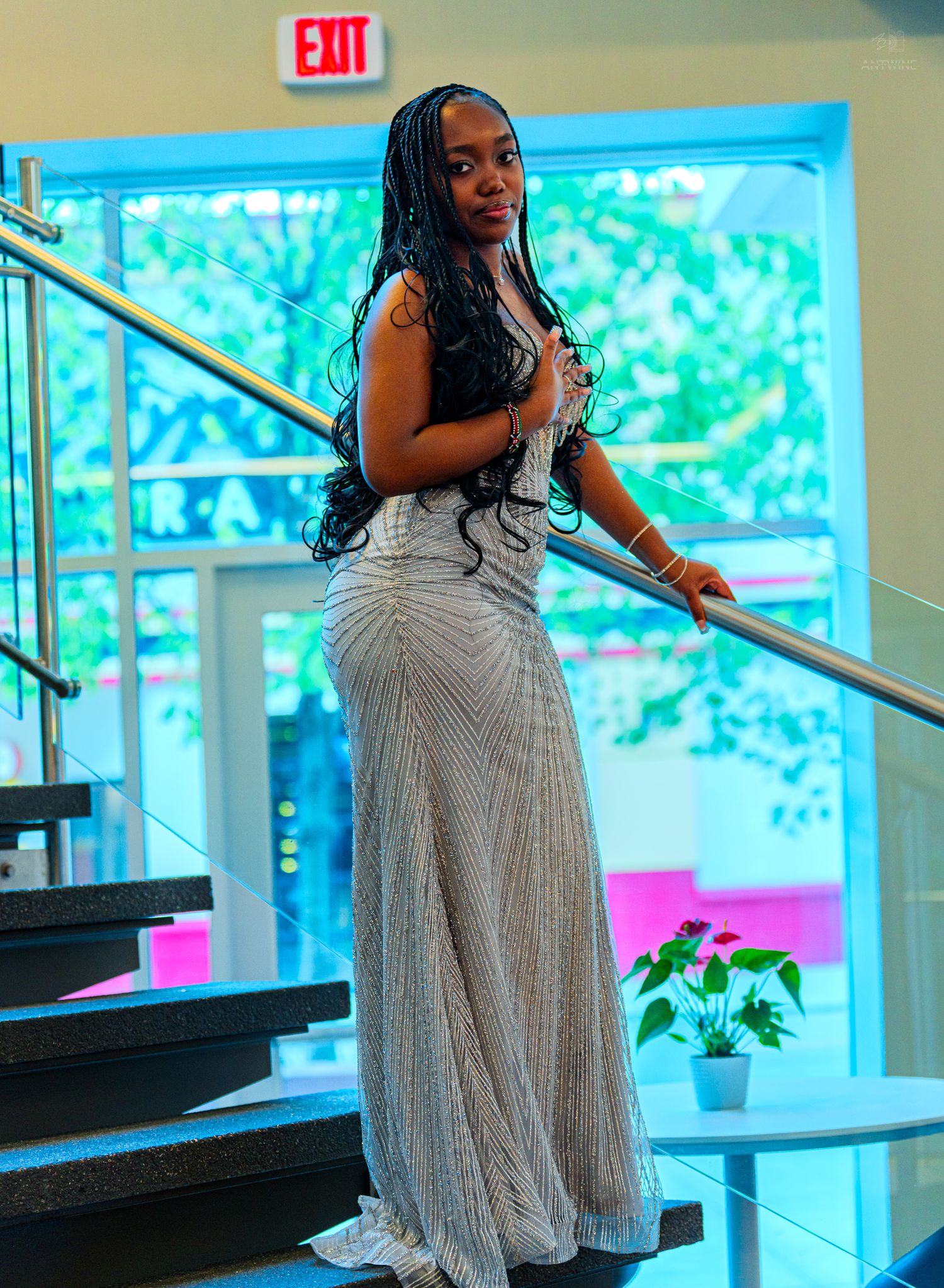 Woman in silver beaded mermaid gown with long braids standing on staircase.