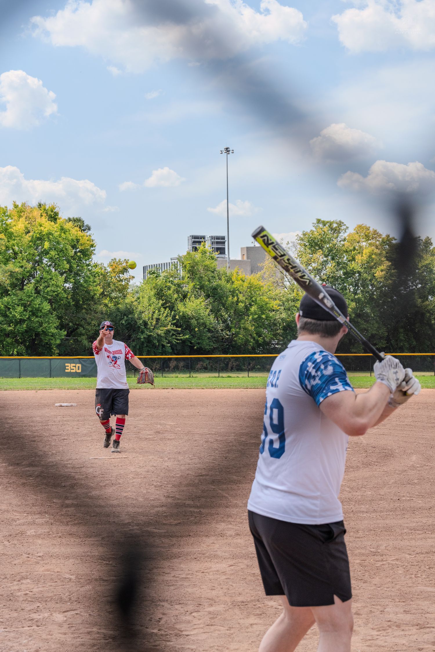 A pitcher winds up to throw as a batter waits at home plate during a softball game.