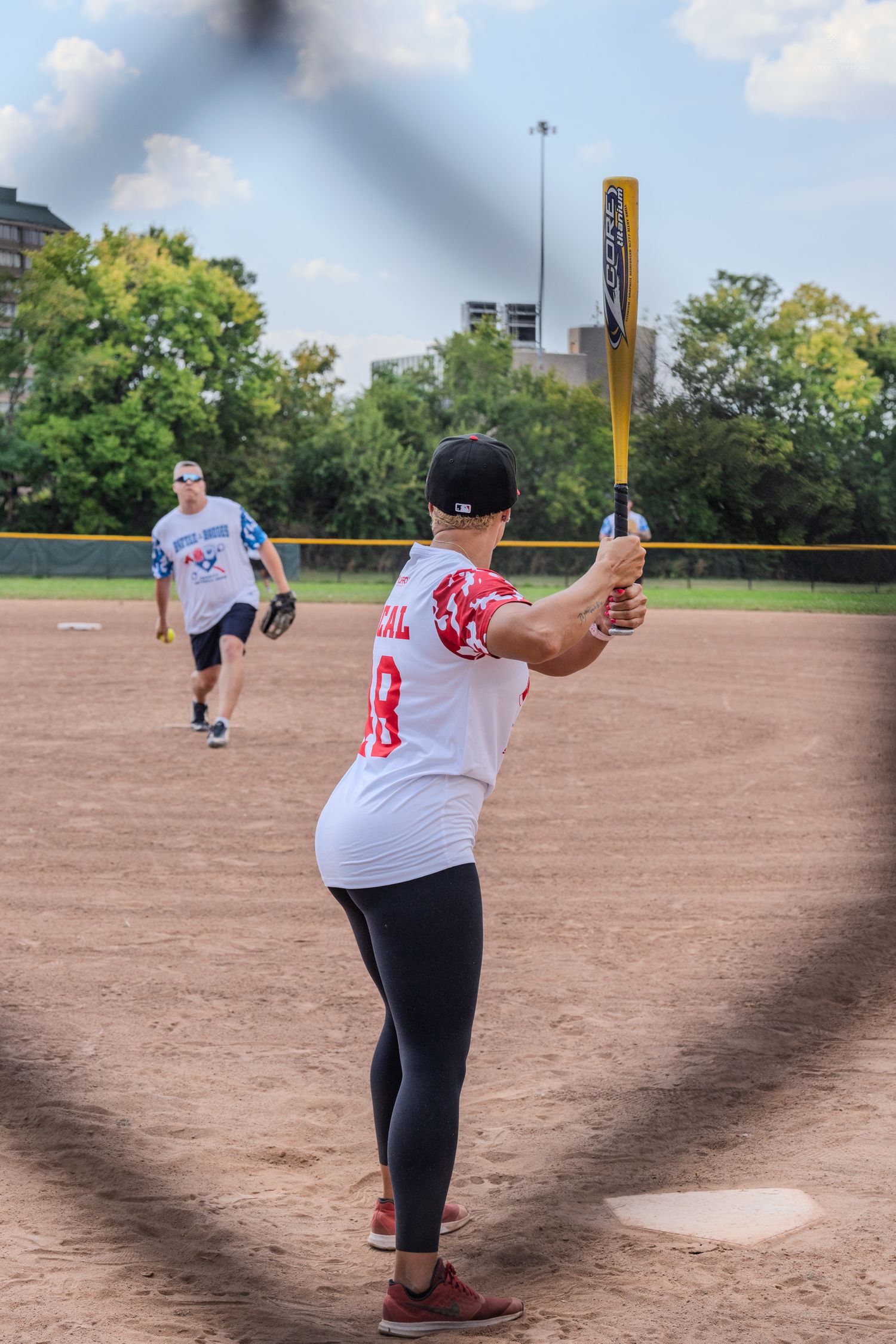Female softball batter in jersey number 18 preparing to swing at an incoming pitch on a dirt field.