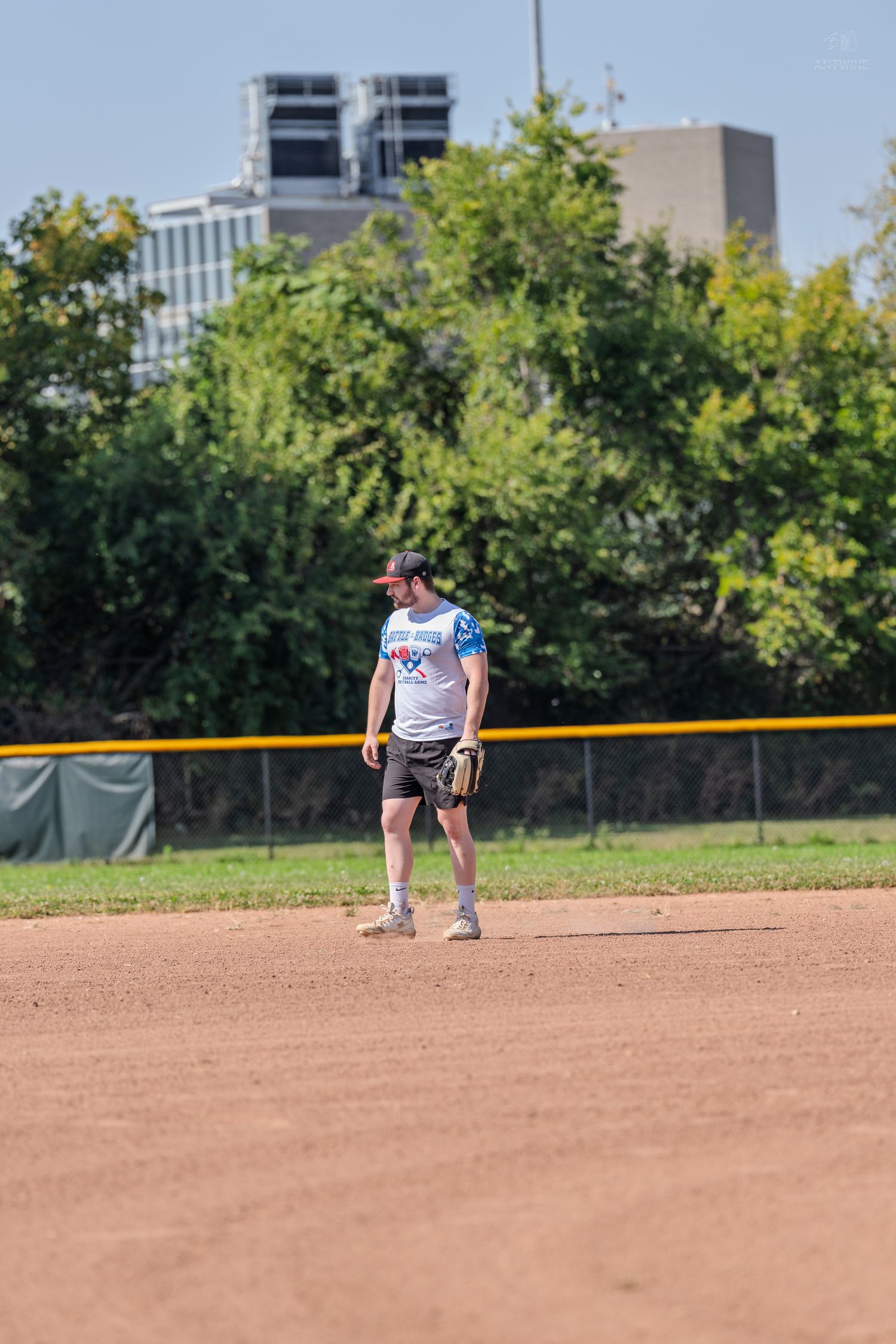 A baseball player stands on the infield dirt wearing a glove during an outdoor recreational game on a sunny day.