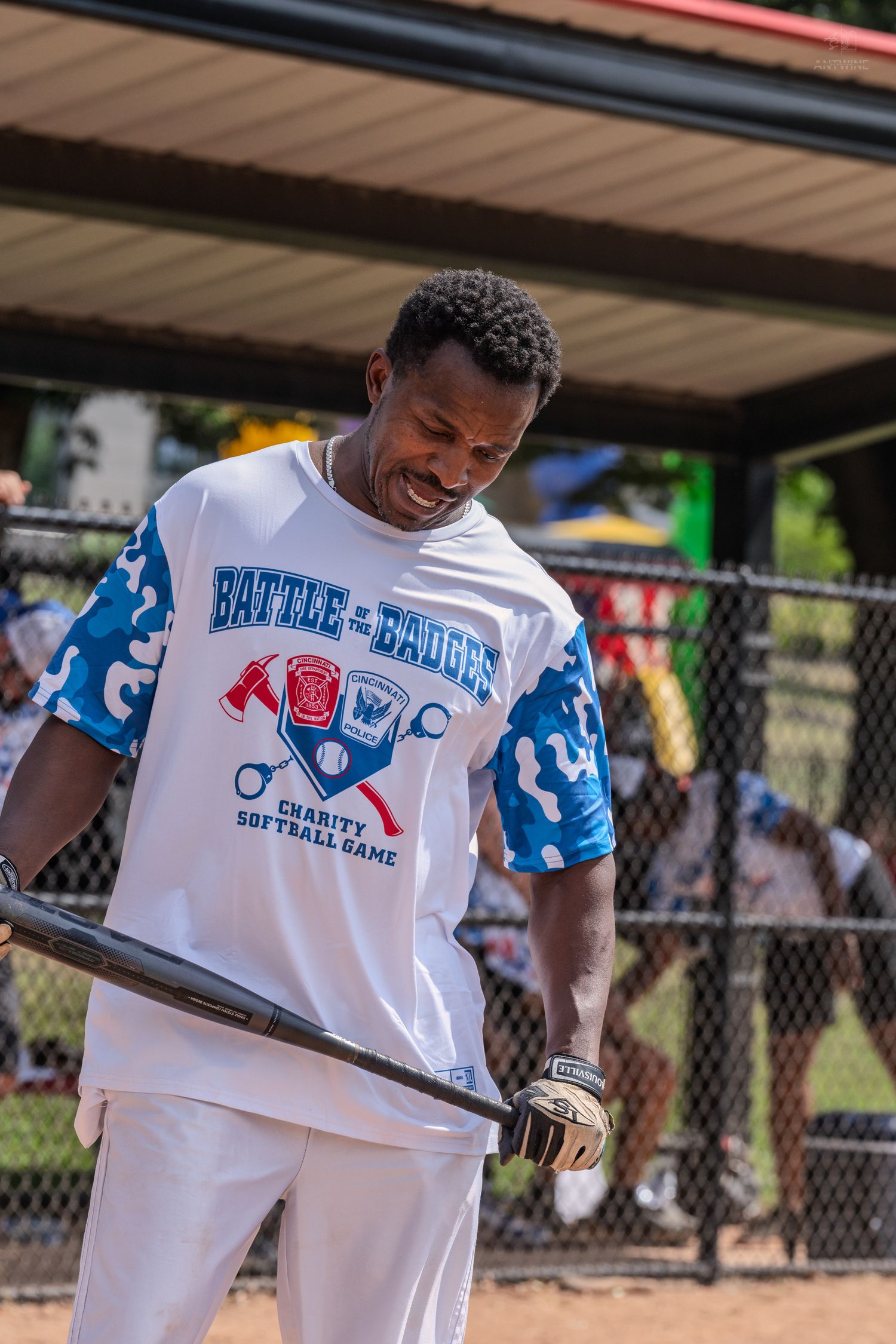 A smiling man holds a bat wearing a Battle of the Badges Charity Softball Game jersey.