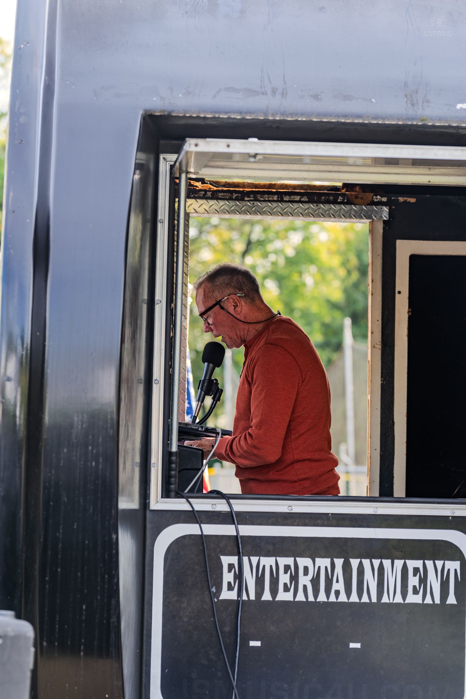 Man in red sweater playing keyboard inside an entertainment truck booth outdoors.
