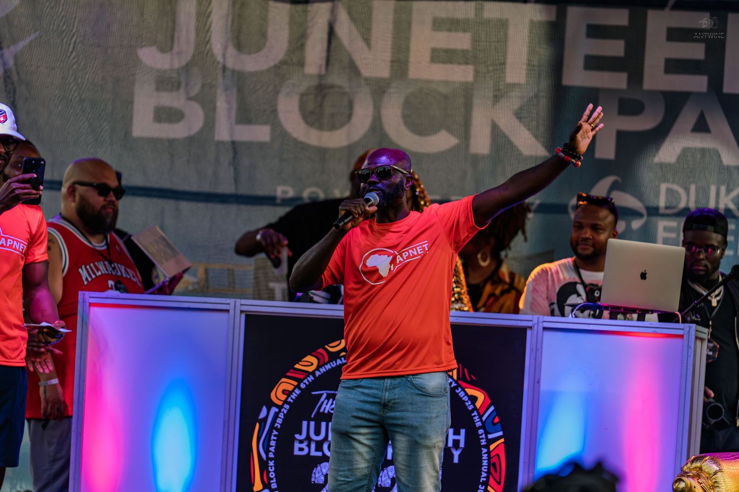 DJ performing energetically on stage at a Juneteenth Block Party celebration at night.
