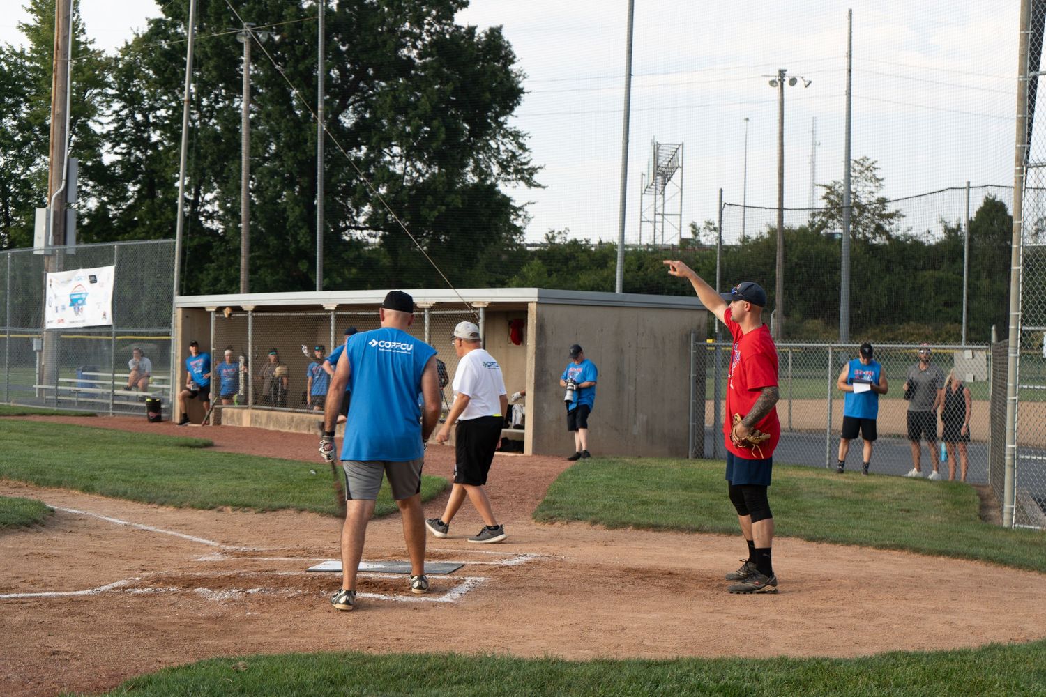 Players gather on a baseball diamond during an outdoor softball game on a sunny day.