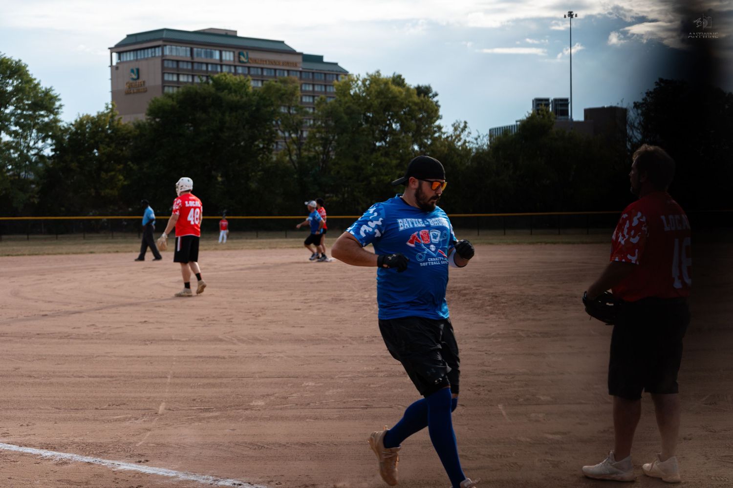 A softball player in a blue jersey runs the bases on a dirt field during a recreational game.