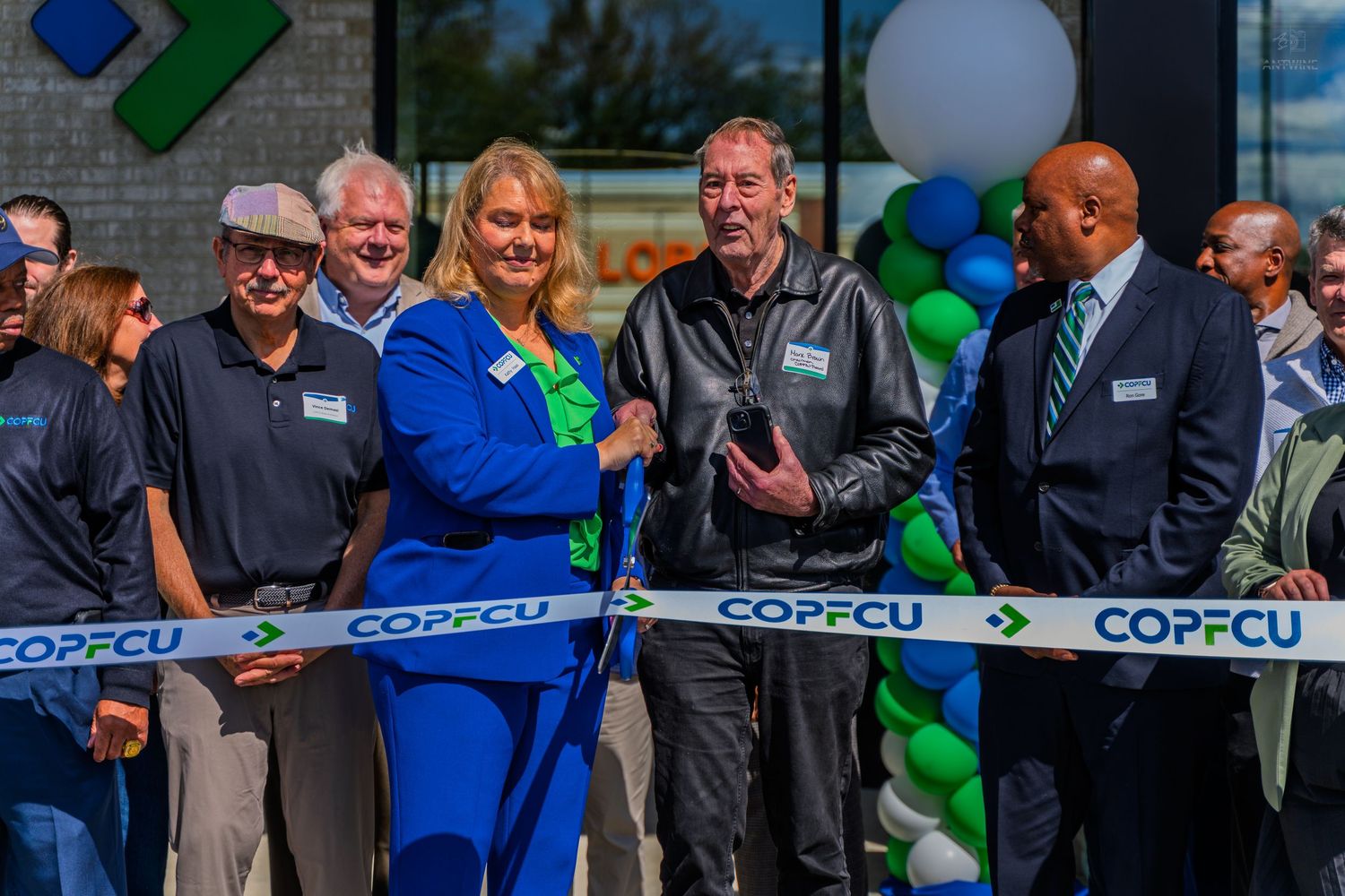 COPFCU credit union ribbon cutting ceremony with smiling officials in front of decorated building with balloons.