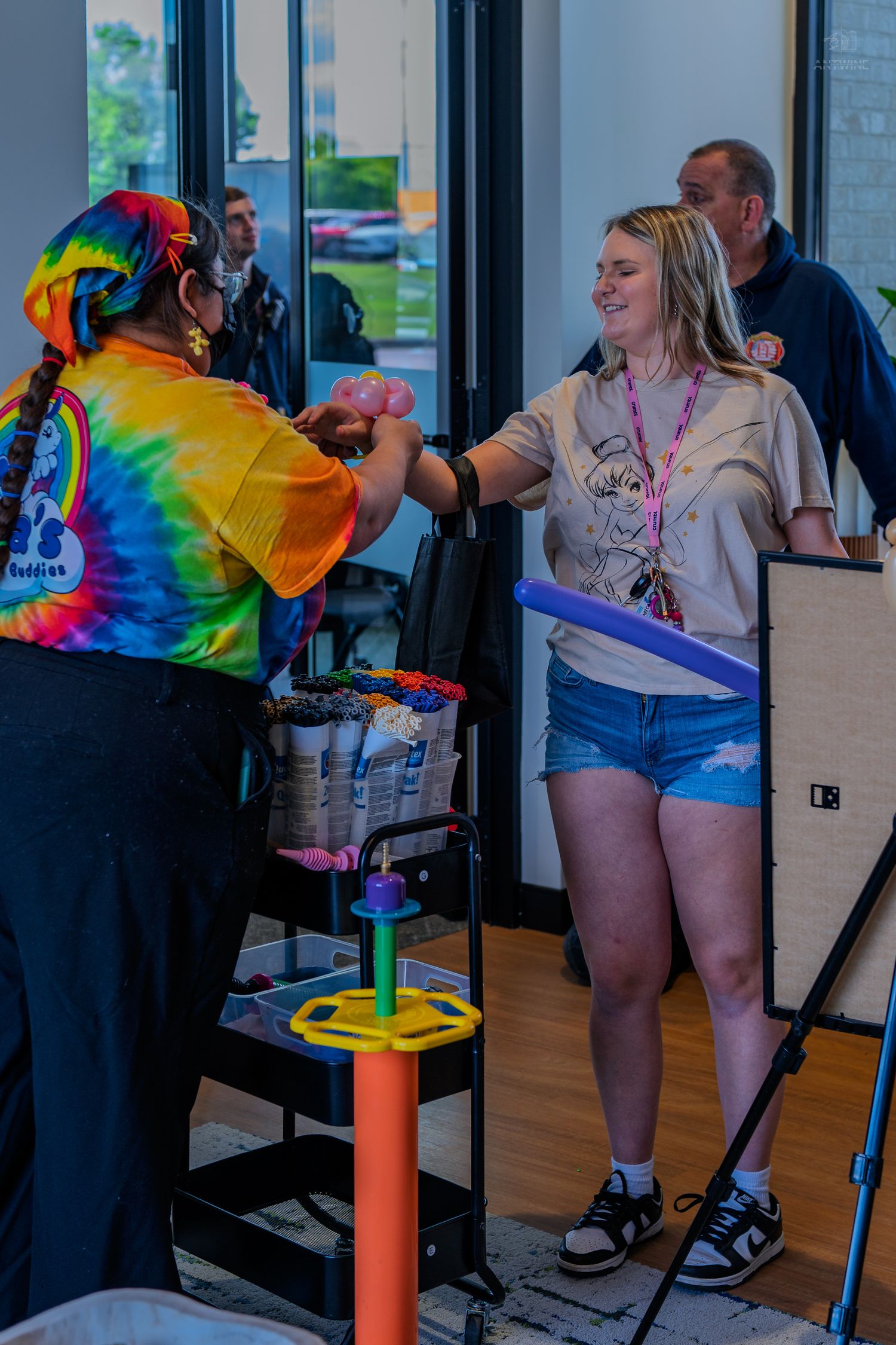 Young woman receiving a balloon animal from a colorful clown at an indoor community event.
