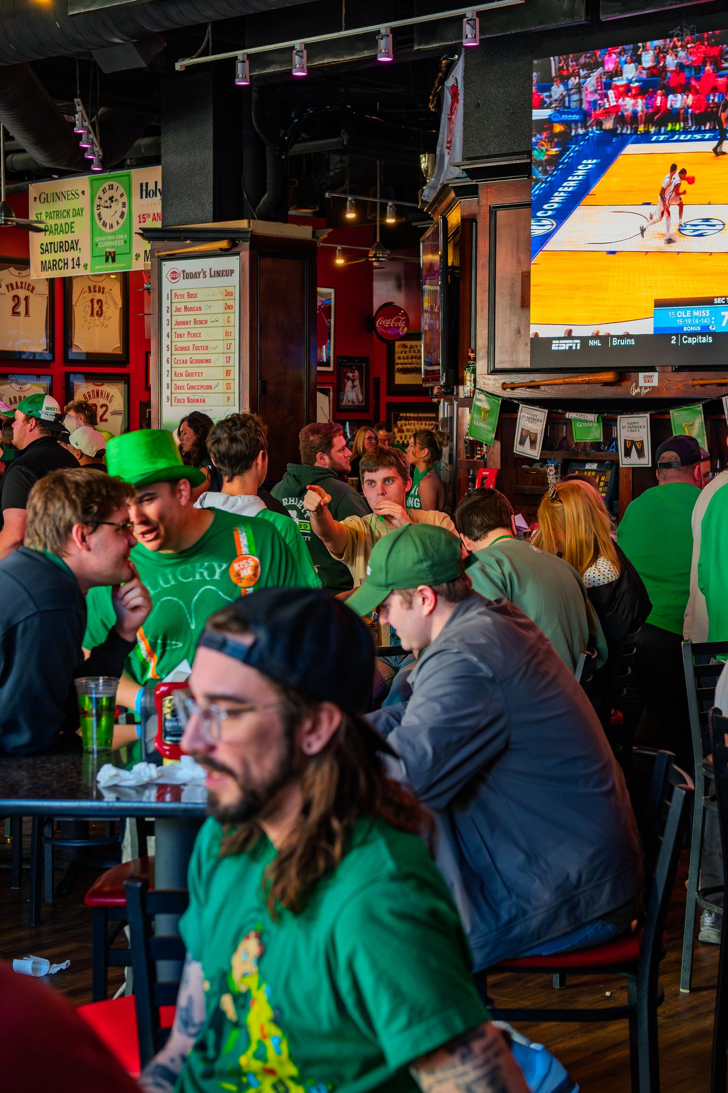 Crowded Irish bar on St. Patrick's Day with patrons in green attire watching basketball on TV.