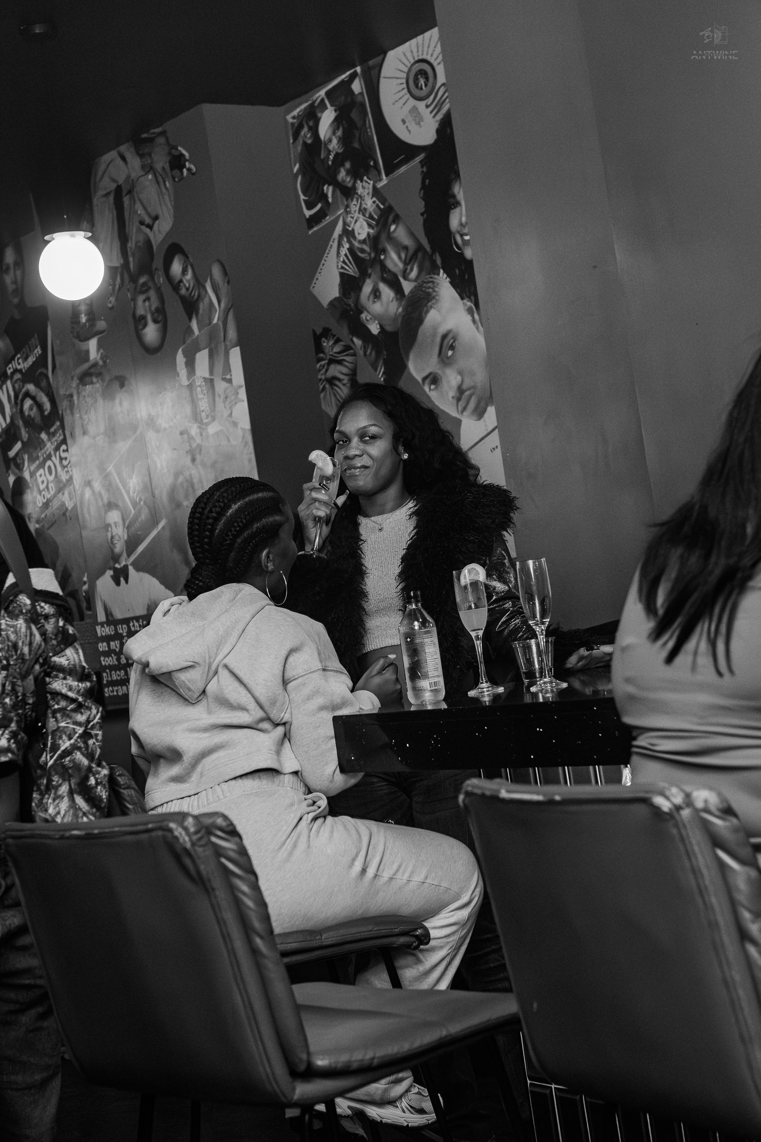 Black and white photo of women socializing at a bar table with champagne glasses in a decorated lounge.