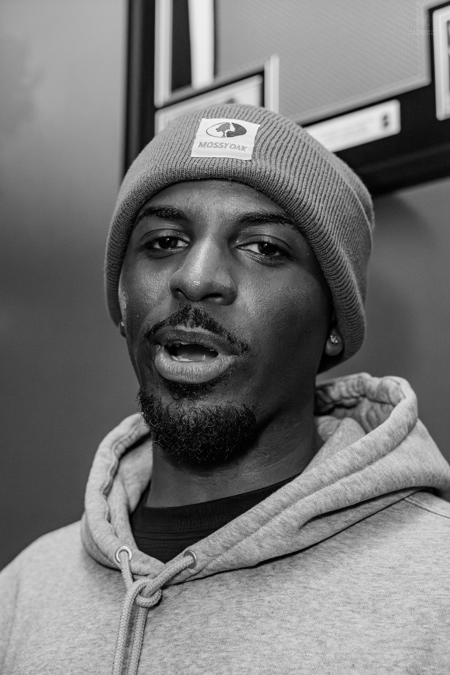 Black and white portrait of a young man wearing a beanie hat and hoodie sweatshirt looking at camera.