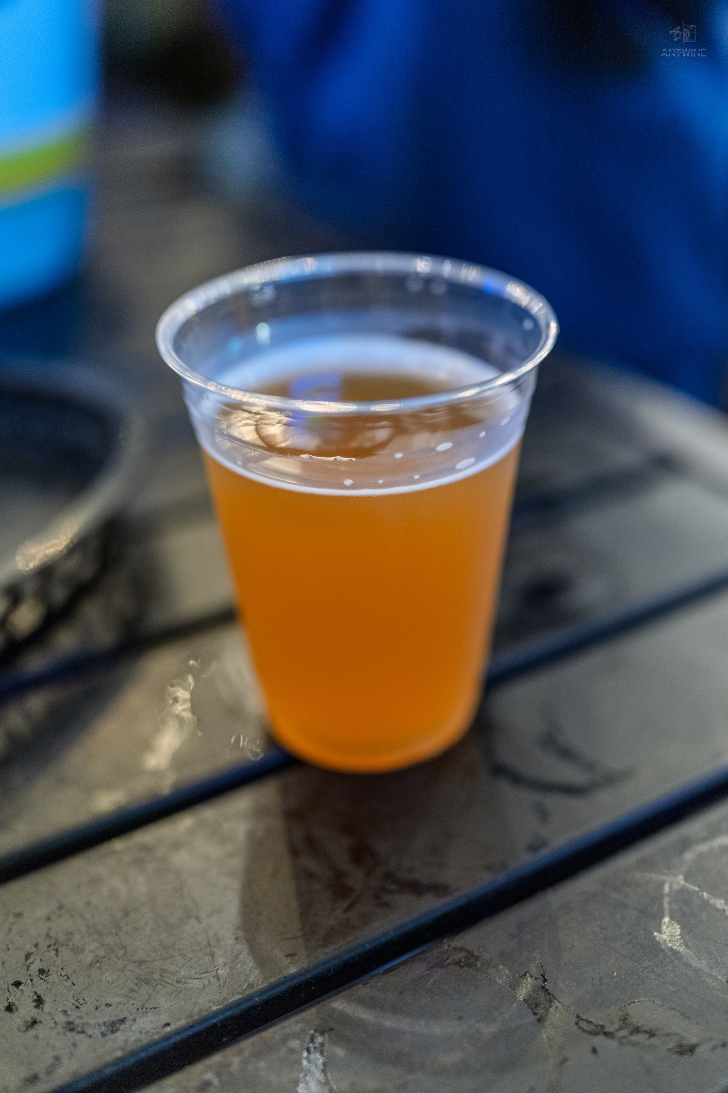 Close-up of a plastic cup filled with golden craft beer on a dark wooden table.