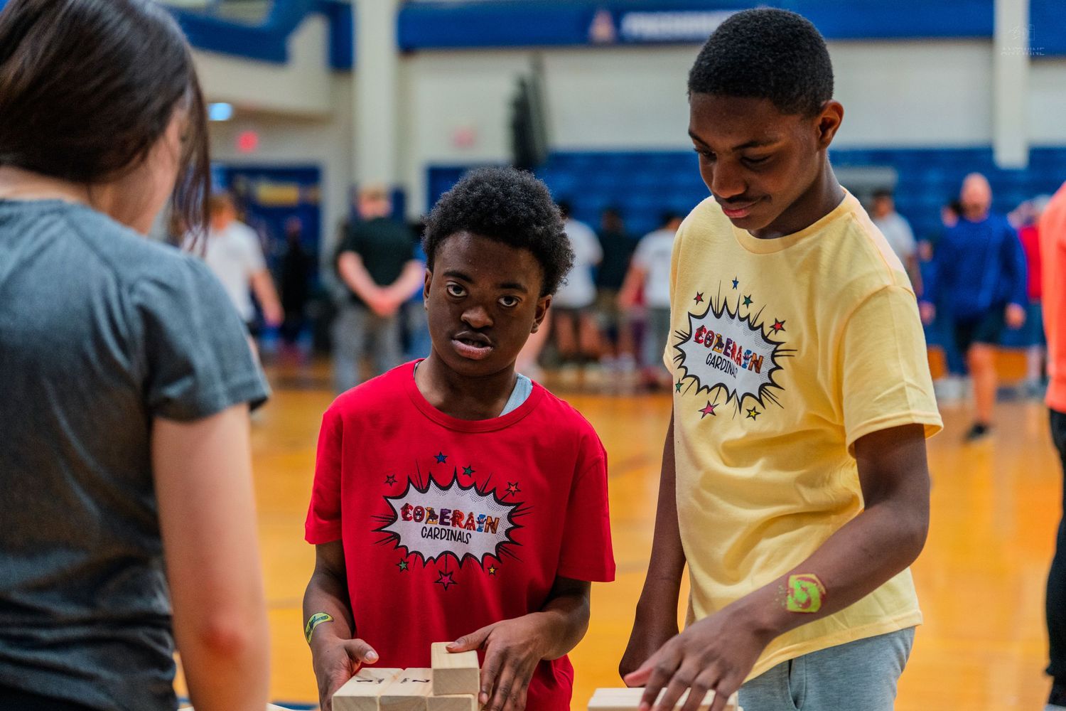 Two young students collaborate on a wooden block activity in a school gymnasium during an educational event.