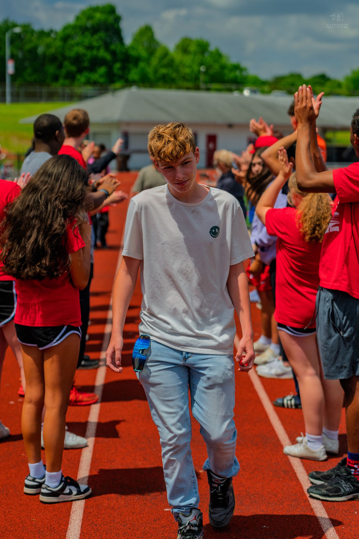 Teen boy walks through a celebratory high-five line on a red track at a school sports event.