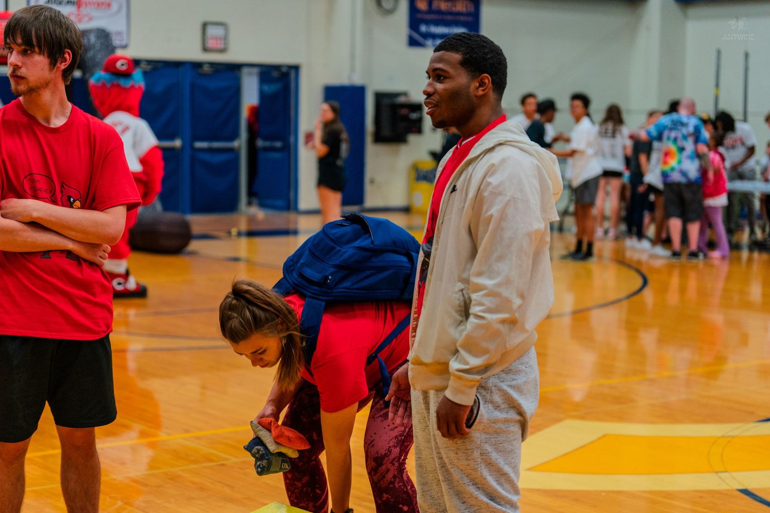 People gathered in a school gymnasium during a sports event, with students in red and gray athletic wear.
