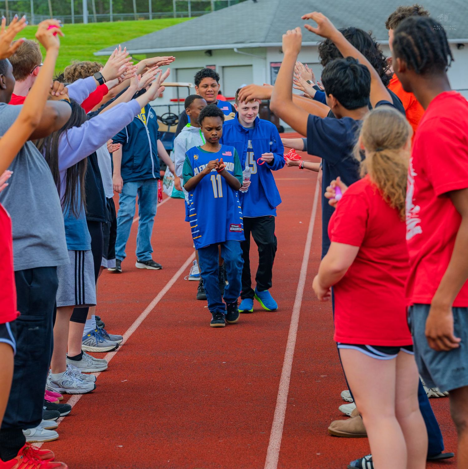 Students form a celebratory tunnel on a red track, high-fiving peers walking through during a school sports event.