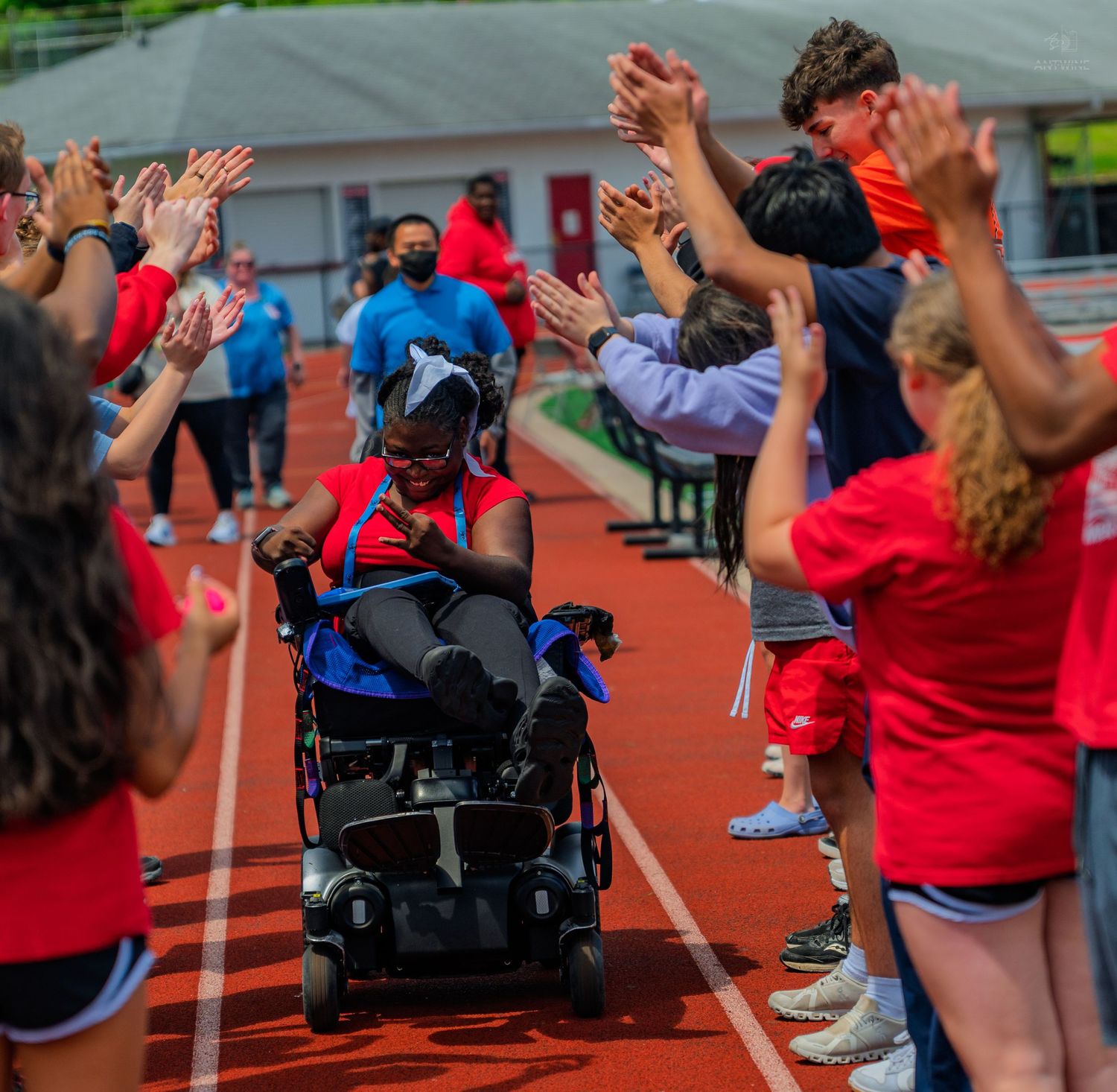 Athlete in wheelchair receives high-fives from cheering crowd on red track during inclusive sports event.