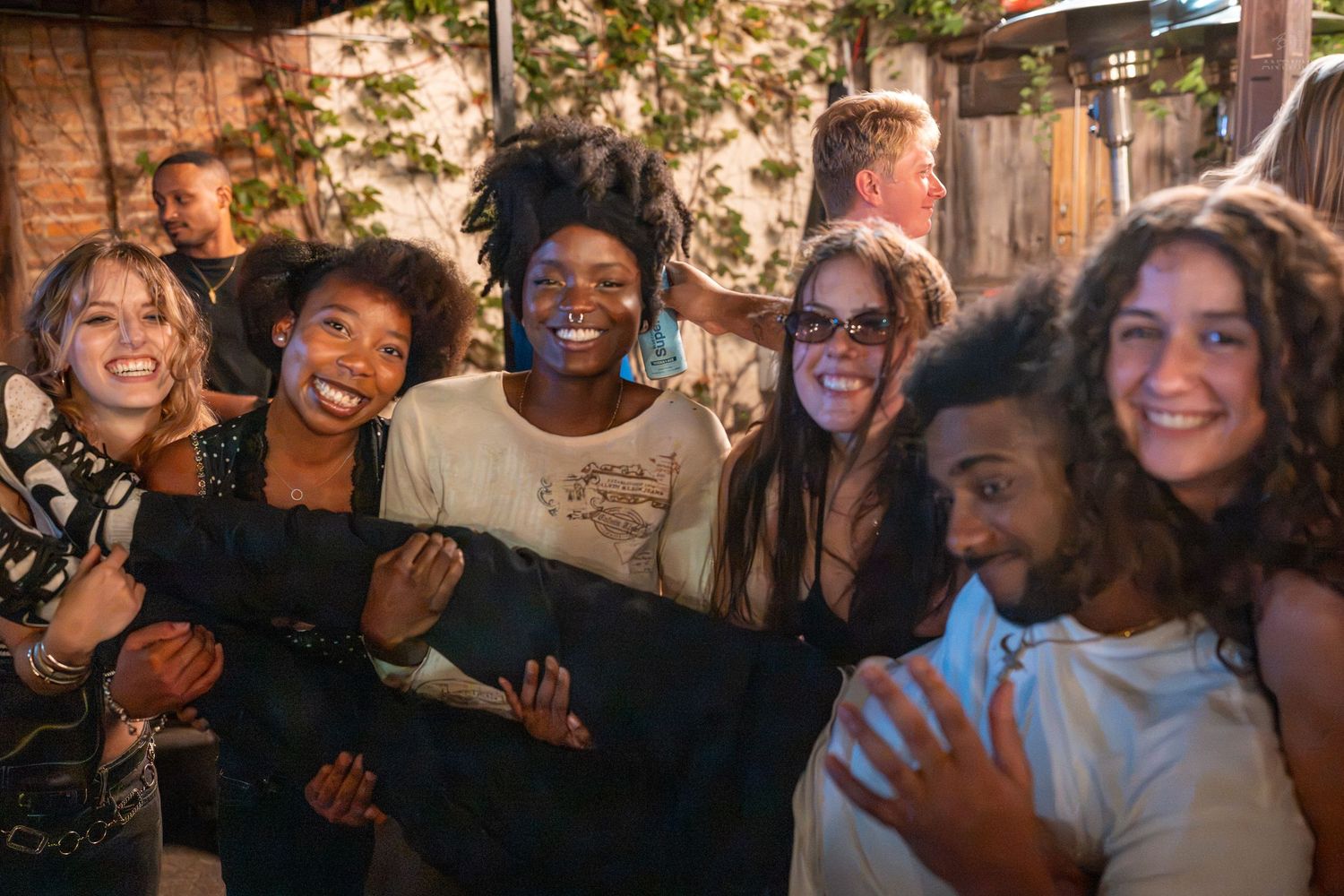 Diverse group of smiling friends posing together at an outdoor party, laughing and embracing in a joyful celebration.