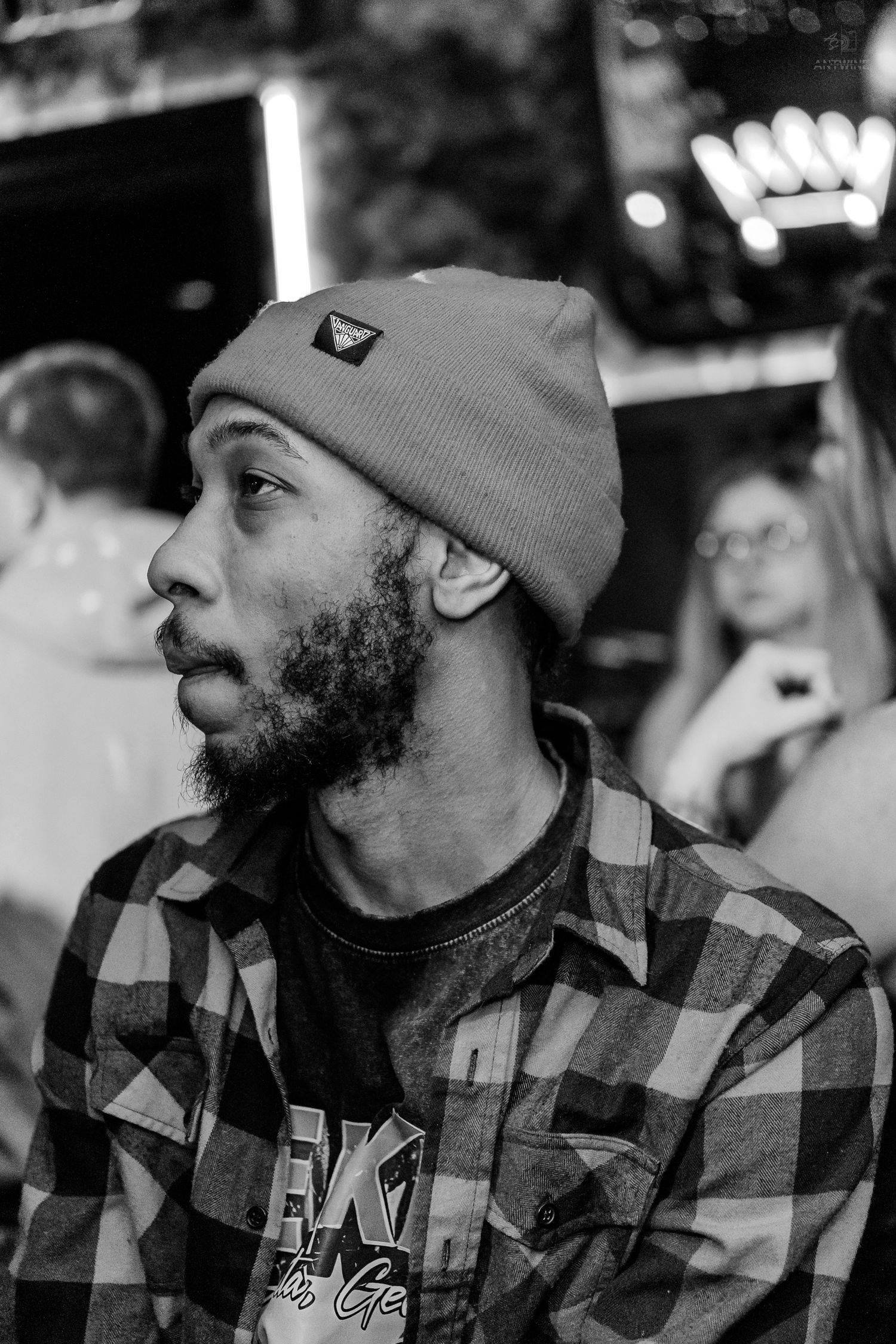 Black and white portrait of a bearded man in a beanie at a nightclub.