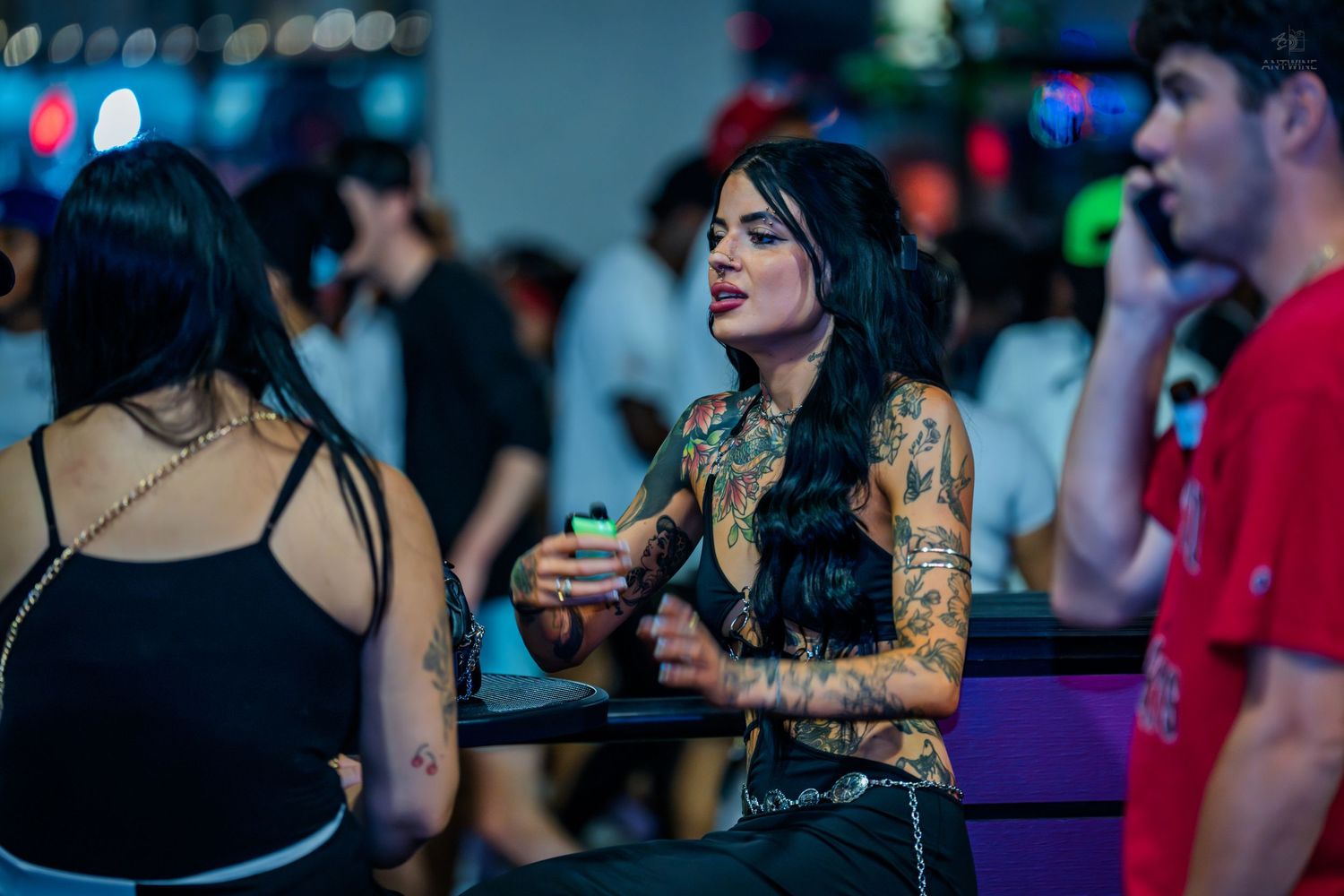 Tattooed woman holding a drink at a dimly lit nightclub event.