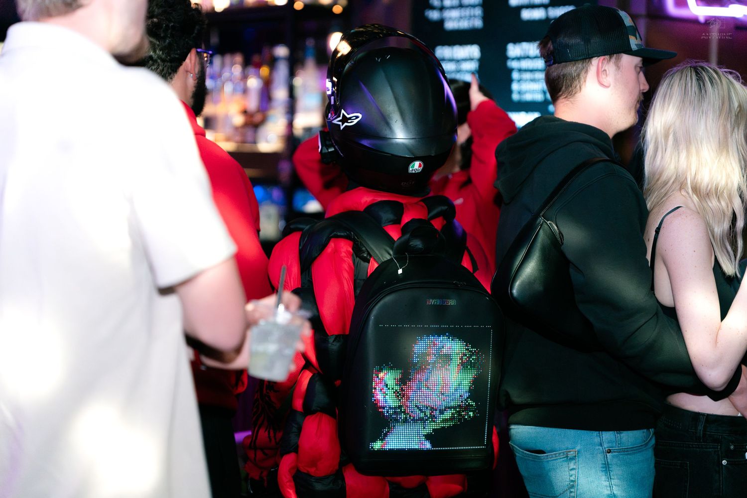 Person in red space suit costume with colorful LED backpack at a crowded bar.