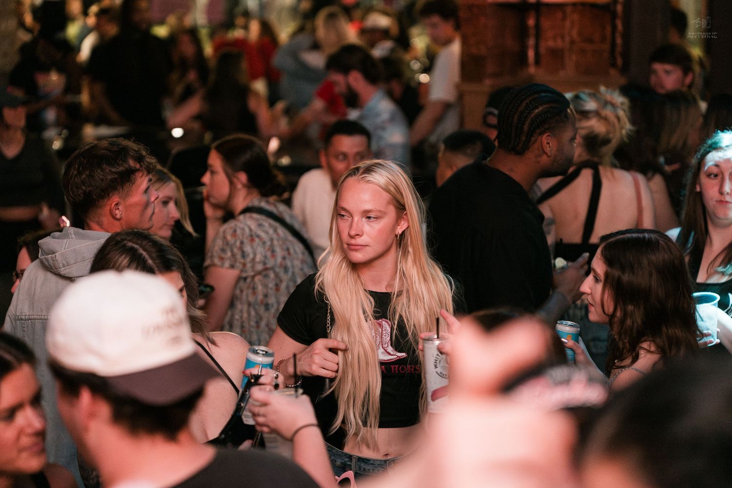 Blonde woman holding a drink surrounded by a crowd at a busy nightclub event.