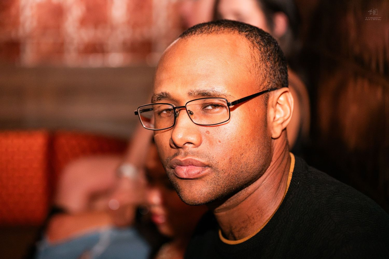 Man wearing glasses with a thoughtful expression at an indoor venue.