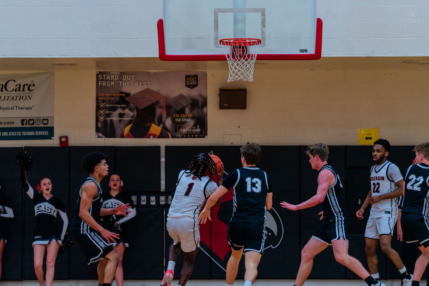 High school basketball players battle under the basket during competitive indoor gymnasium game.