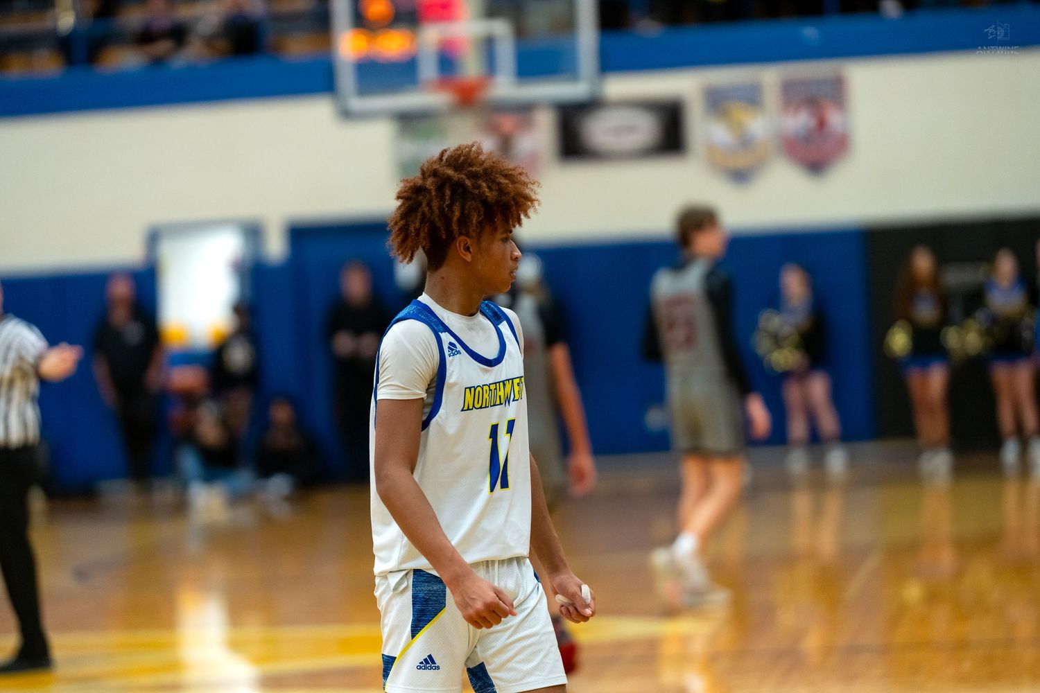 High school basketball player wearing number 11 blue and gold uniform walks on gymnasium court.