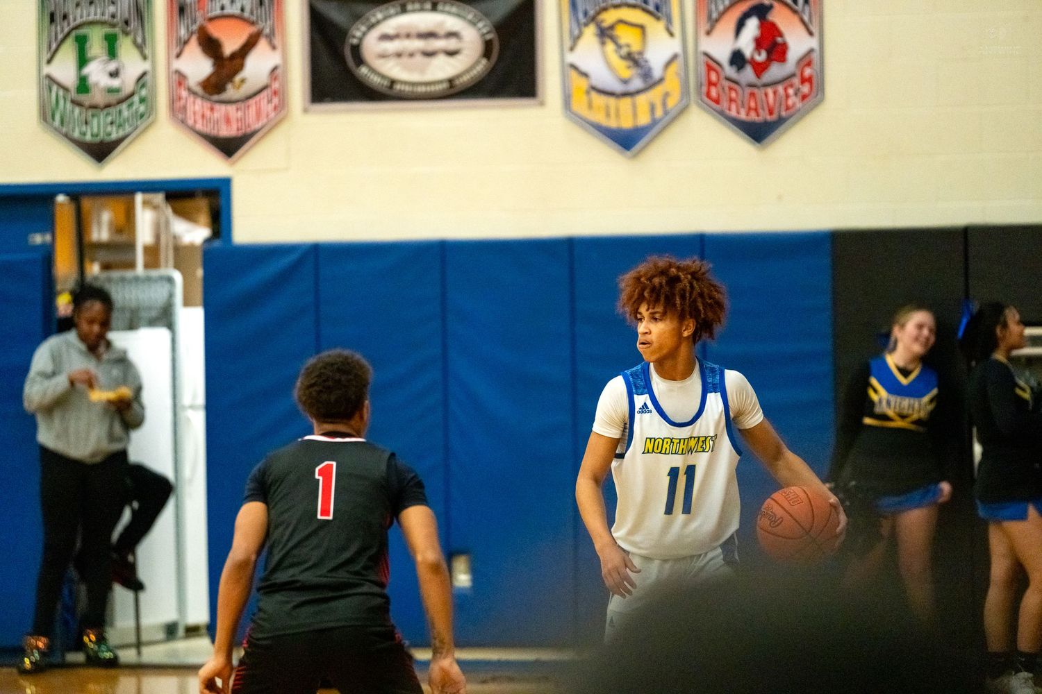 High school basketball player number 11 in blue dribbles the ball while being guarded by opponent number 1 in black.