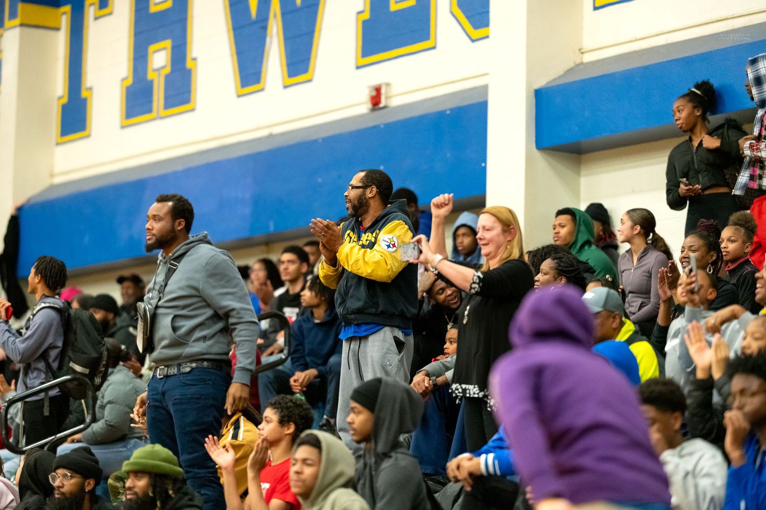 Energetic crowd of fans cheering and celebrating at a high school basketball game in a packed gym.