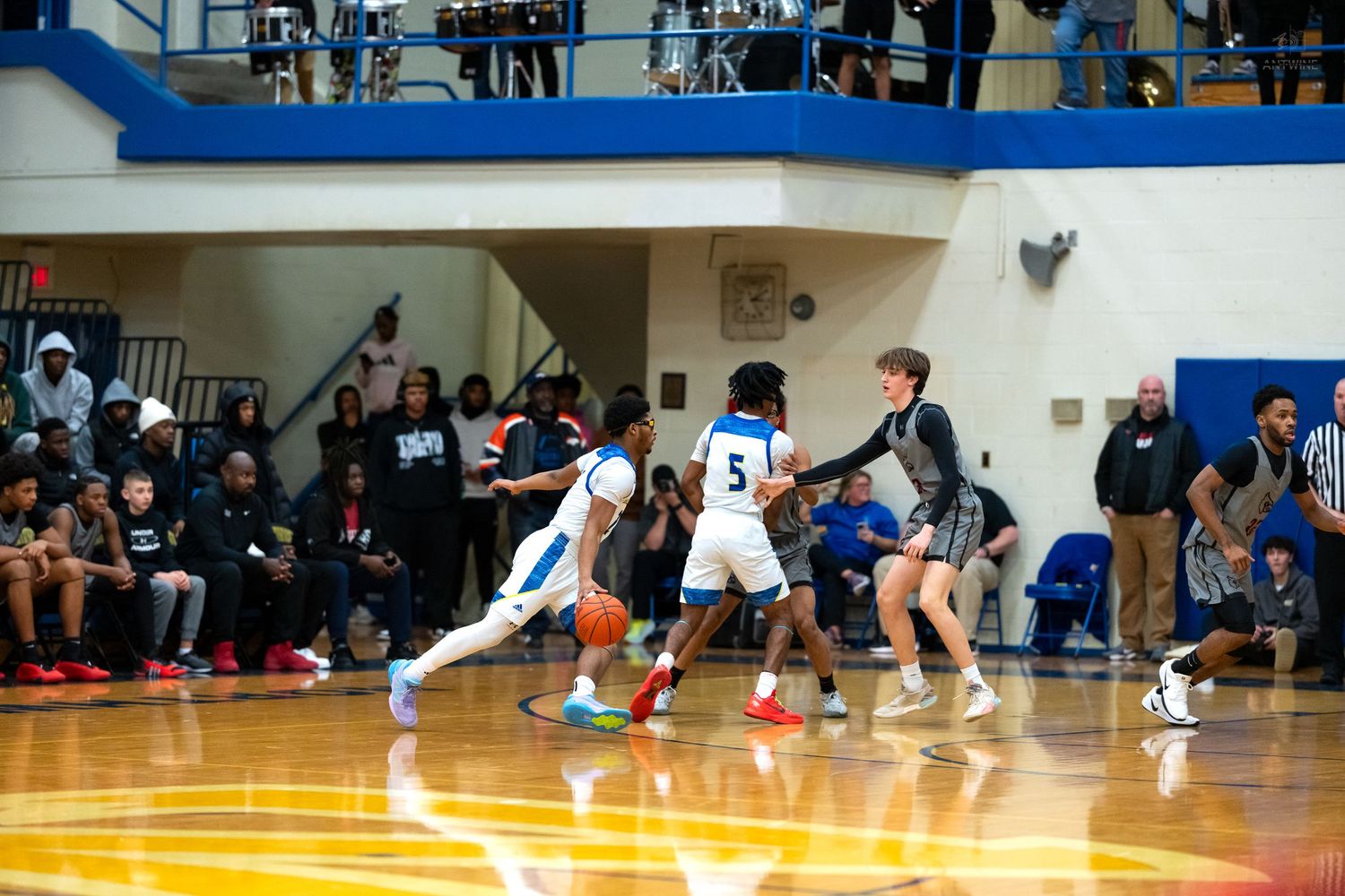 Basketball player number 5 in white dribbles the ball while being defended during a high school gym game.