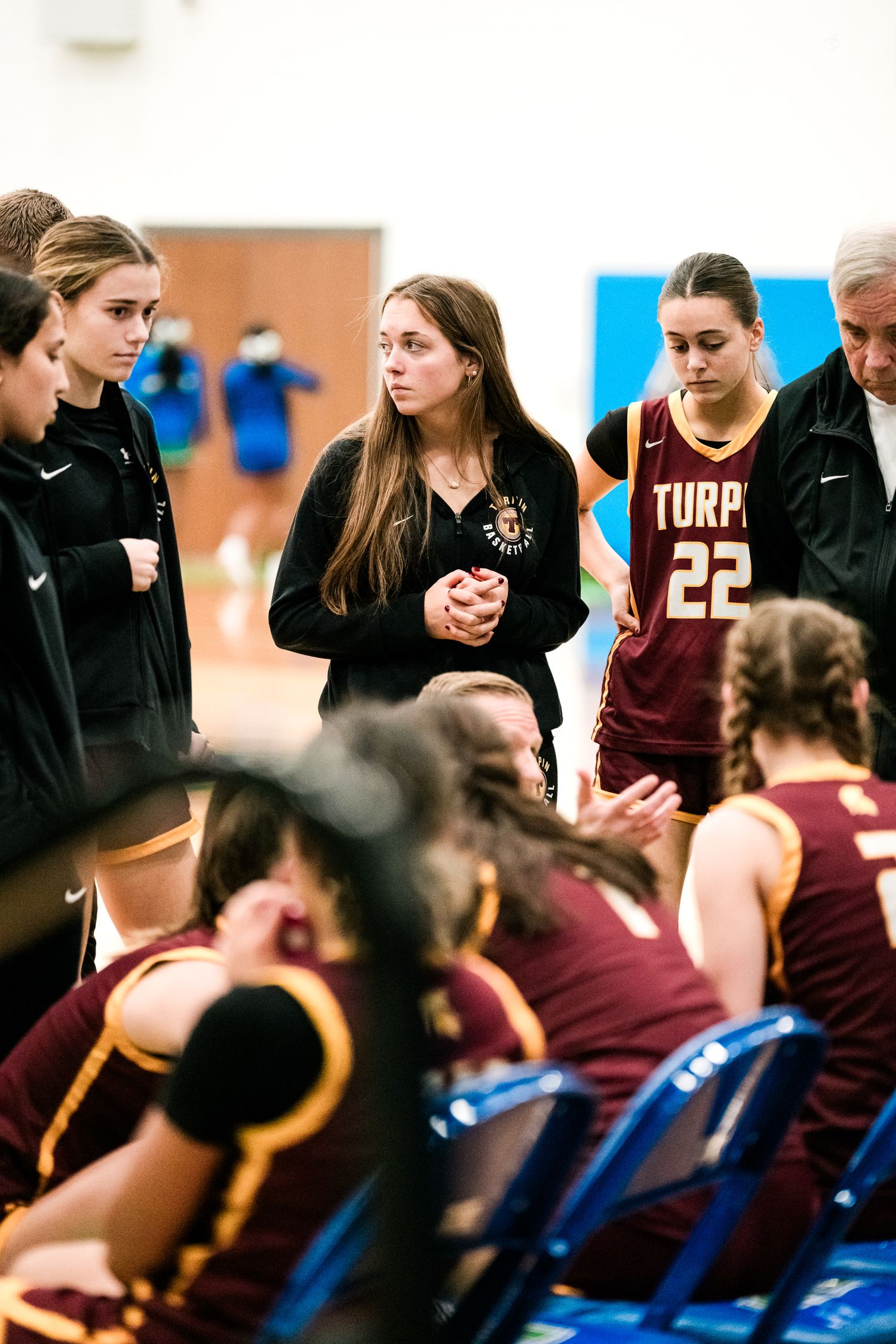Turpin girls basketball team huddles during timeout with coaches in maroon uniforms at high school game.