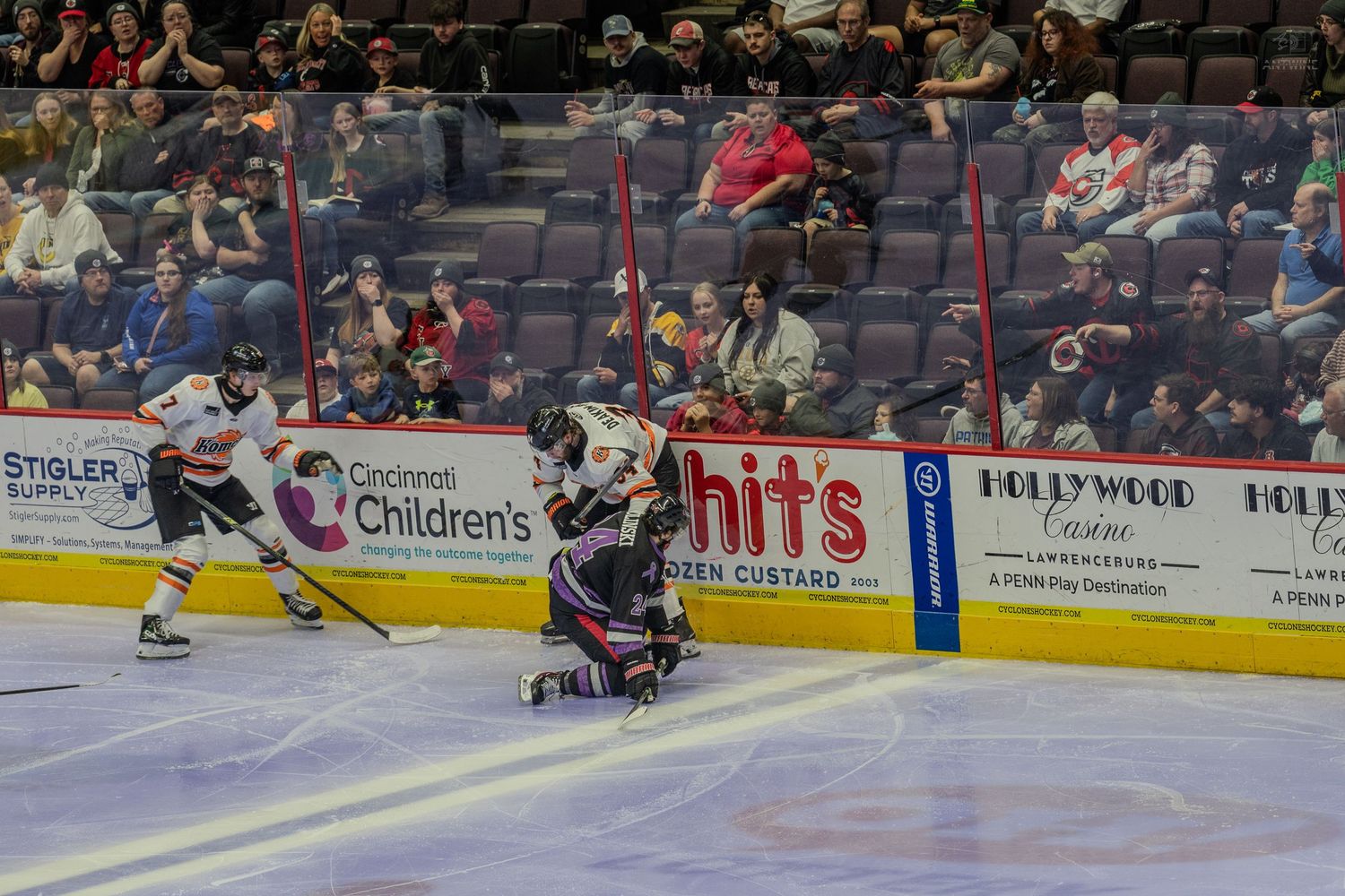 Hockey player falls to the ice during an intense minor league hockey game with fans watching.
