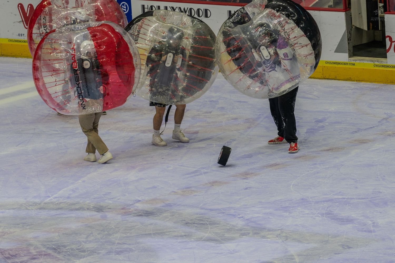 Three participants in inflatable bubble balls chase a puck on ice during a fun intermission activity.