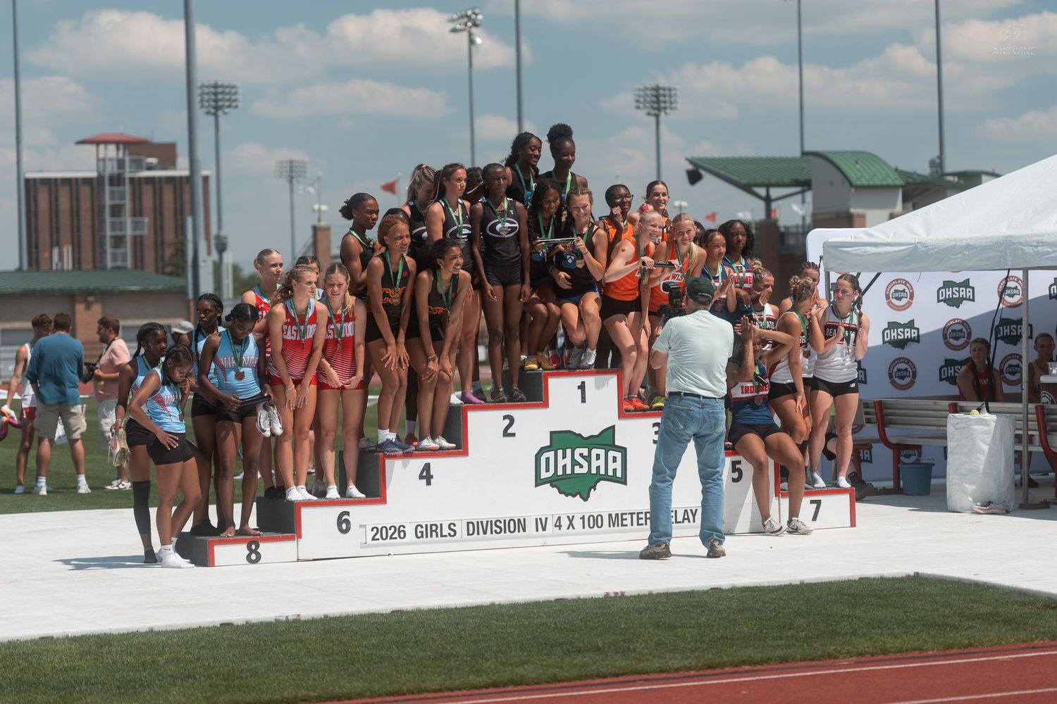 Multiple girls relay teams posing on OHSAA Girls Division IV 4x100 Meter Relay championship awards podium.